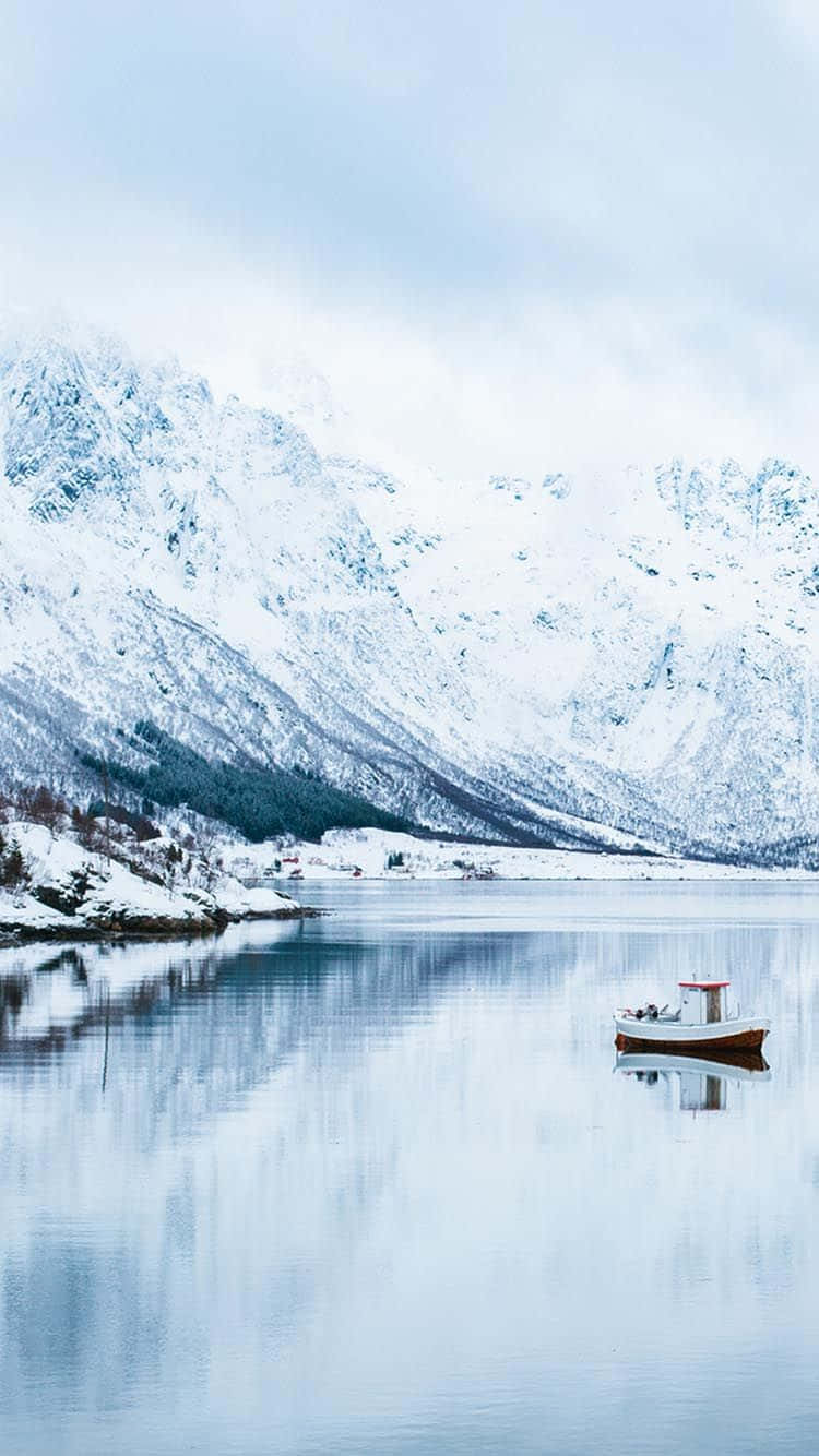 Norway 桌布 壁紙 — 一艘孤獨的木船在如鏡的冬日湖上靜靜漂浮，四周是白雪覆蓋的高聳山脈，天空蒼白。