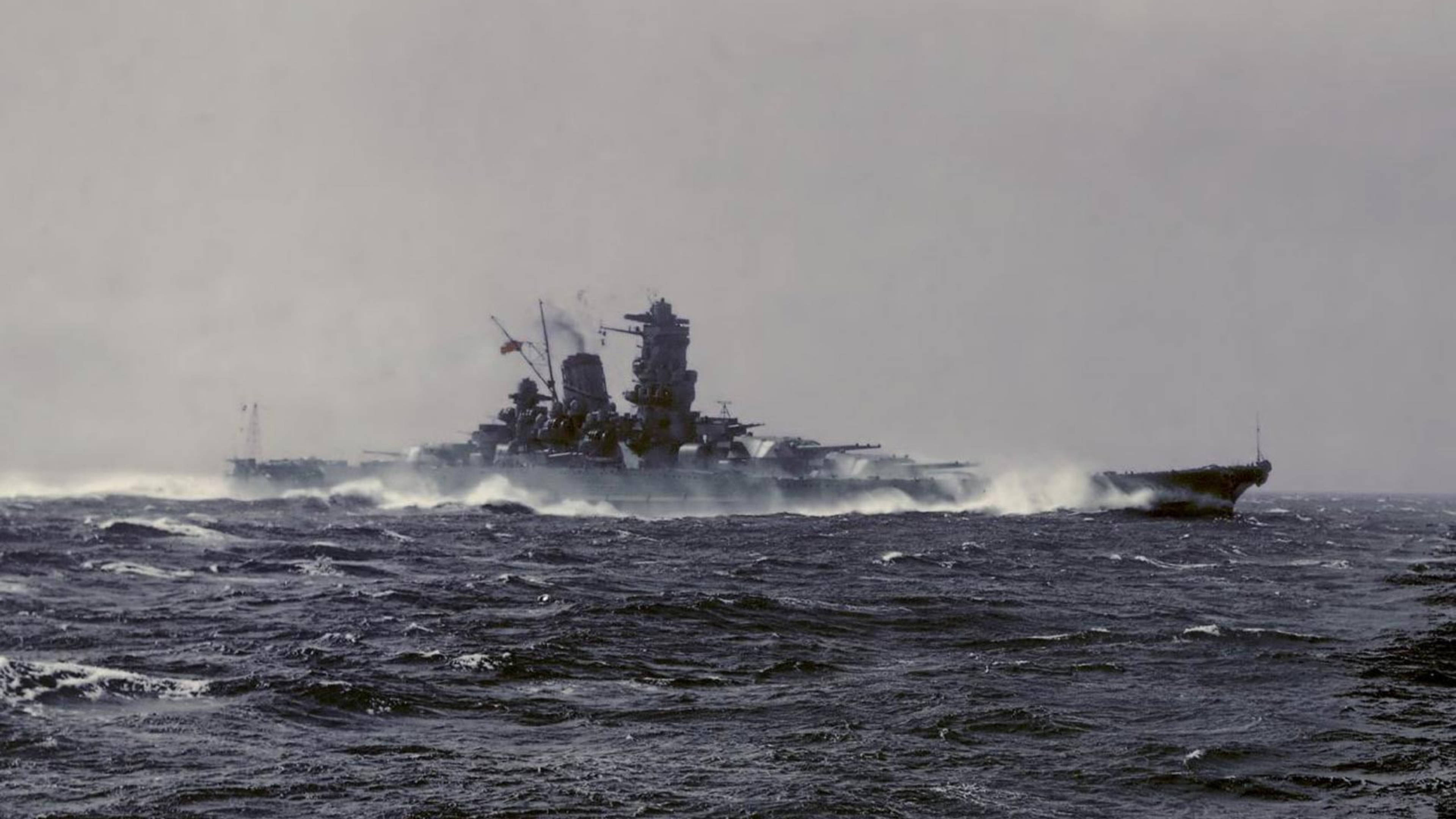 Japanese 桌布 壁紙 — 一艘巨大的戰艦在陰天之下劃過波濤洶湧的黑暗海水，留下泡沫般的尾跡。