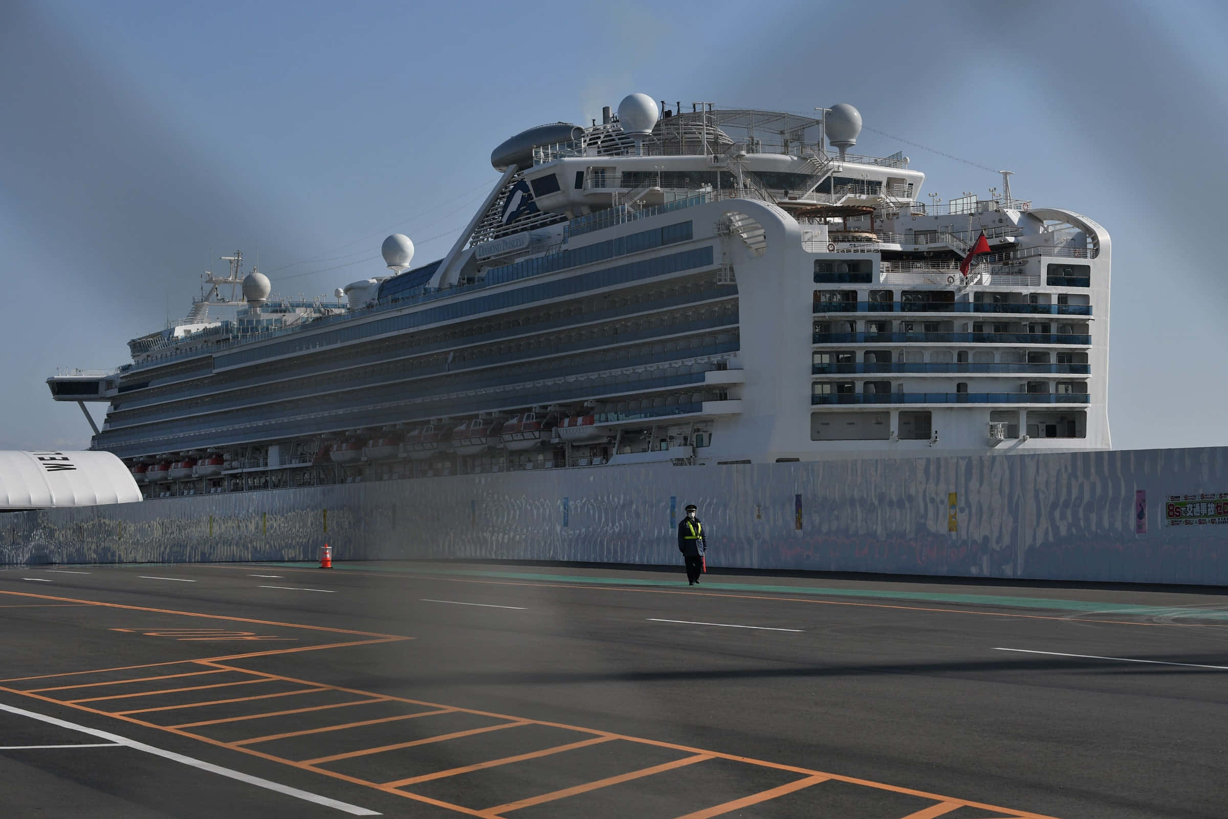 Cruise Ship 桌布 壁紙 — 一艘巨大的白色郵輪停靠在港口，前景瀝青地面上站著一名孤獨的保安。