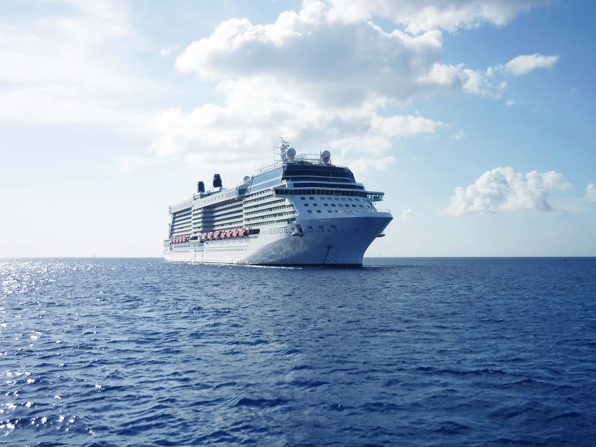 Cruise Ship 桌布 壁紙 — 一艘巨大的白色郵輪在明亮的天空下，伴隨著蓬鬆的雲朵，在深藍色的海洋上平靜地航行。