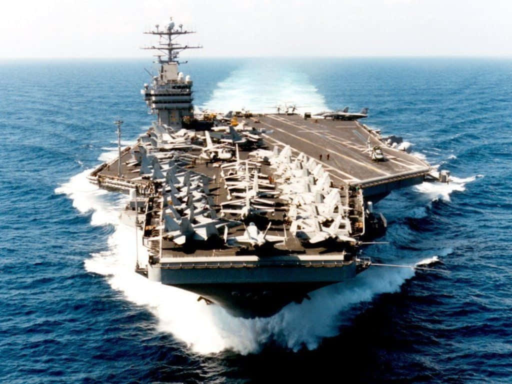 Navy 桌布 壁紙 — 一艘巨大的航空母艦在深藍色的海浪中破浪前行，戰鬥機在明亮的日光下整齊排列在甲板上。