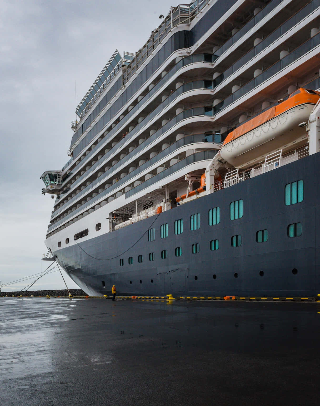 Cruise Ship 桌布 壁紙 — 一艘巨大的郵輪，船身深色，閃爍著青綠色的窗戶，在陰天停靠在濕漉漉的碼頭。