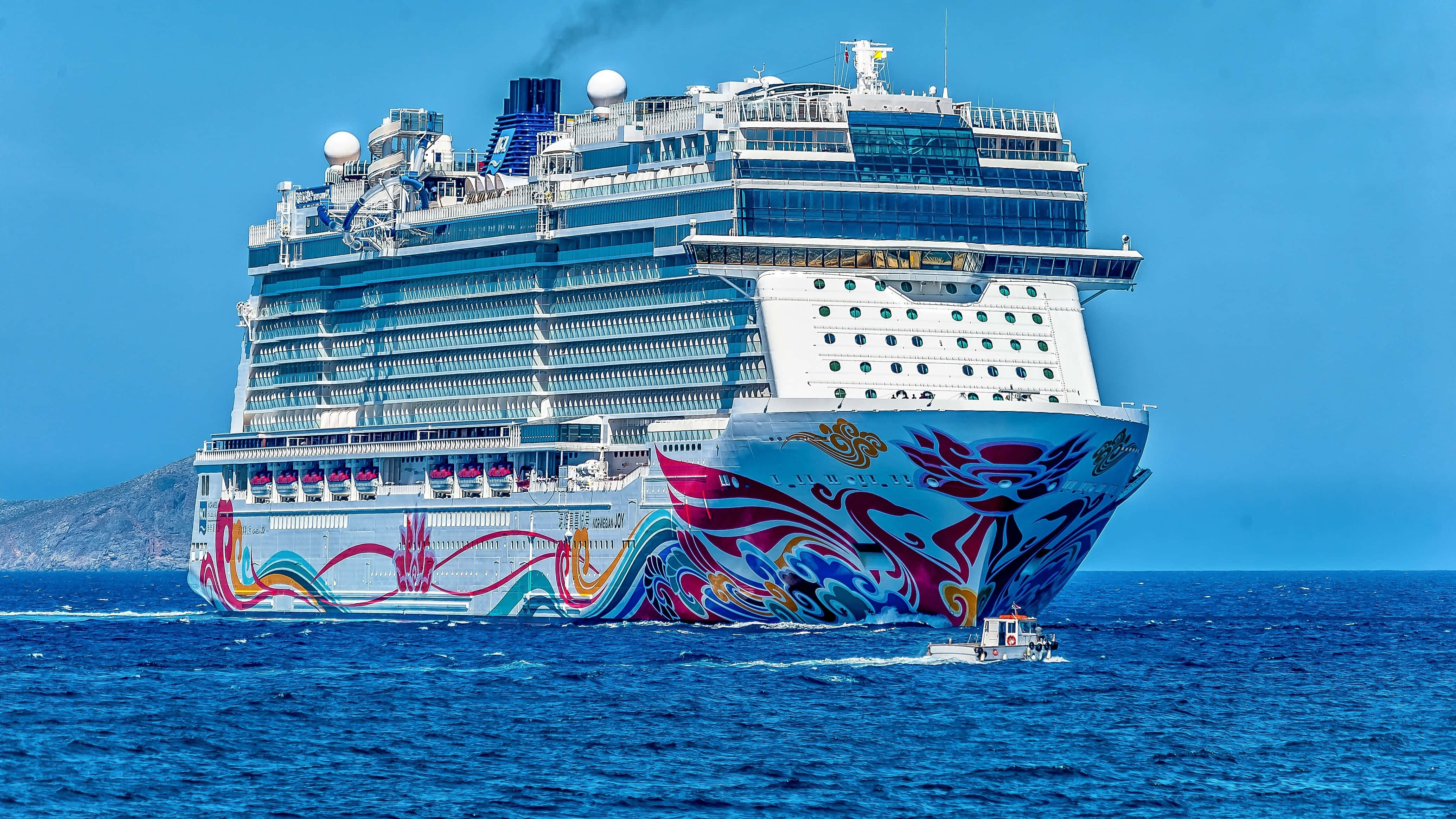Cruise Ship 桌布 壁紙 — 一艘巨大的郵輪，飾有充滿活力的龍主題藝術品，在晴朗的天空下航行於深藍色的海洋中。