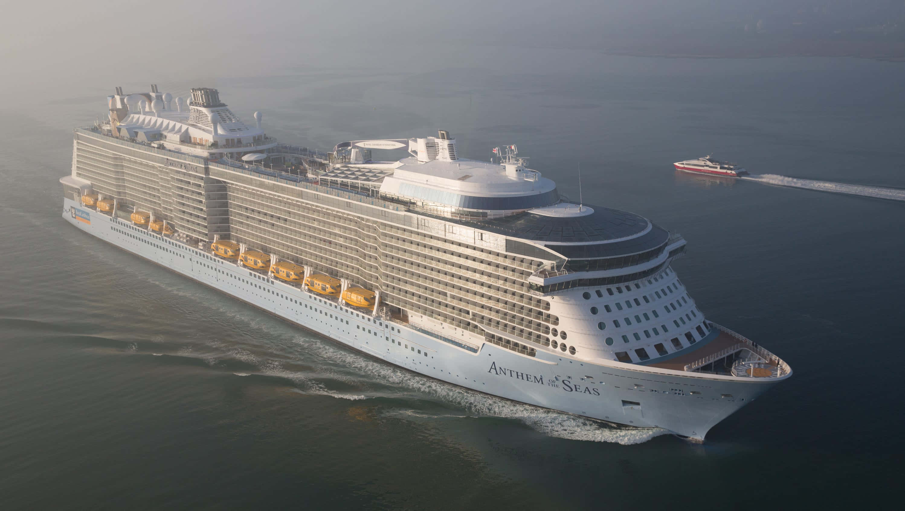 Cruise Ship 桌布 壁紙 — 一艘巨大的郵輪海洋聖歌號平靜地航行在霧氣瀰漫的海洋中，後面跟著一艘小型快艇。