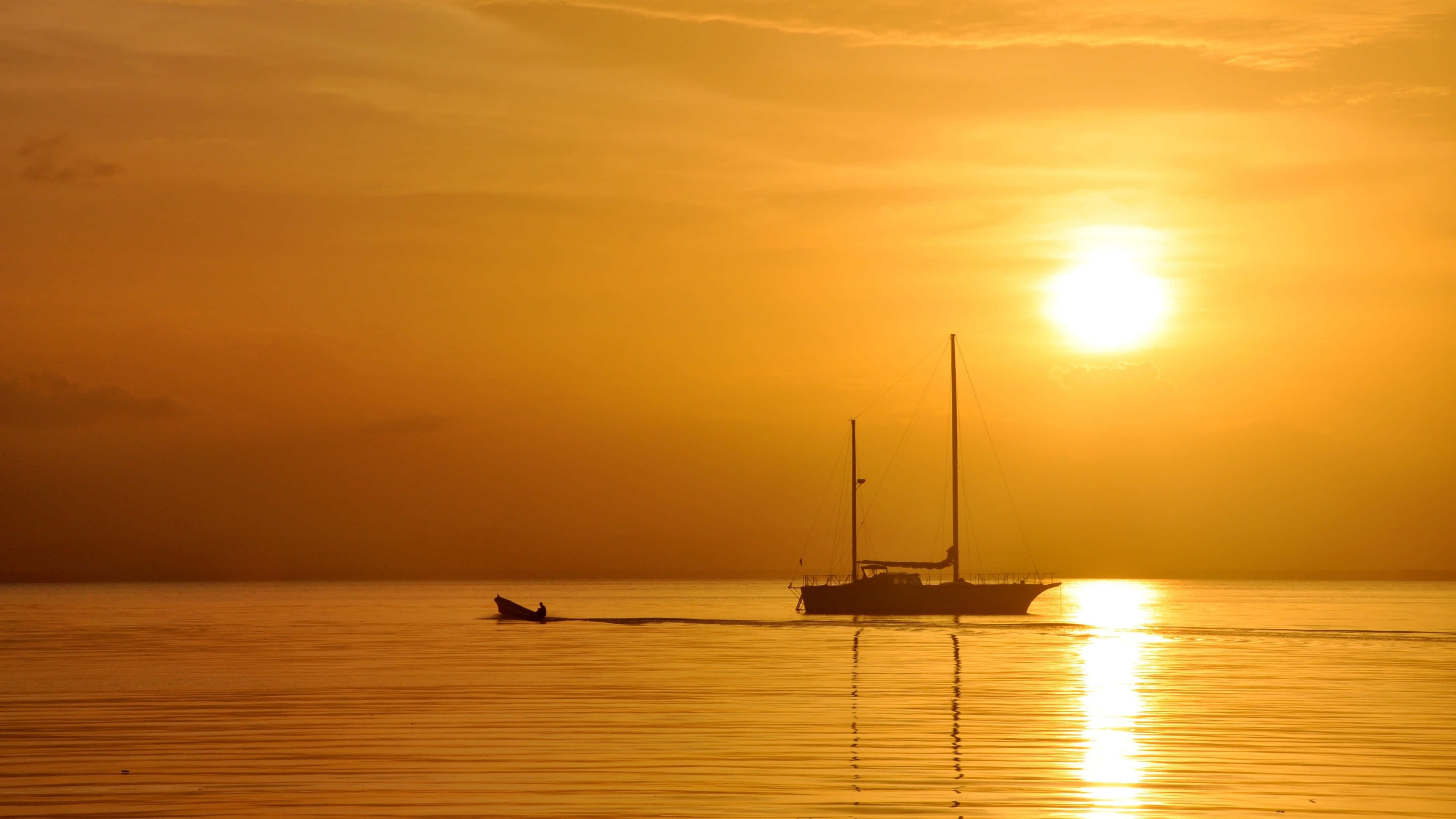 Boating 桌布 壁紙 — 一艘帆船和一艘小船在平靜的水面上滑行，夕陽在火紅的橙色天空中落下。
