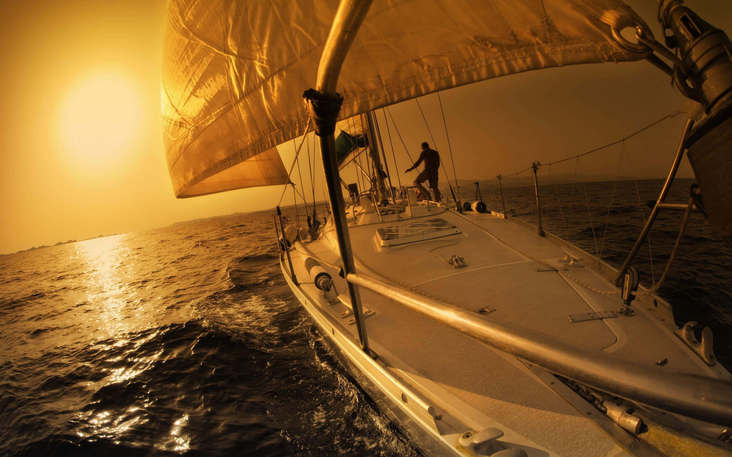 Yacht 桌布 壁紙 — 一艘帆船在金色水域中滑行，夕陽在它身後落下，為帆船和海面投下溫暖的光芒。