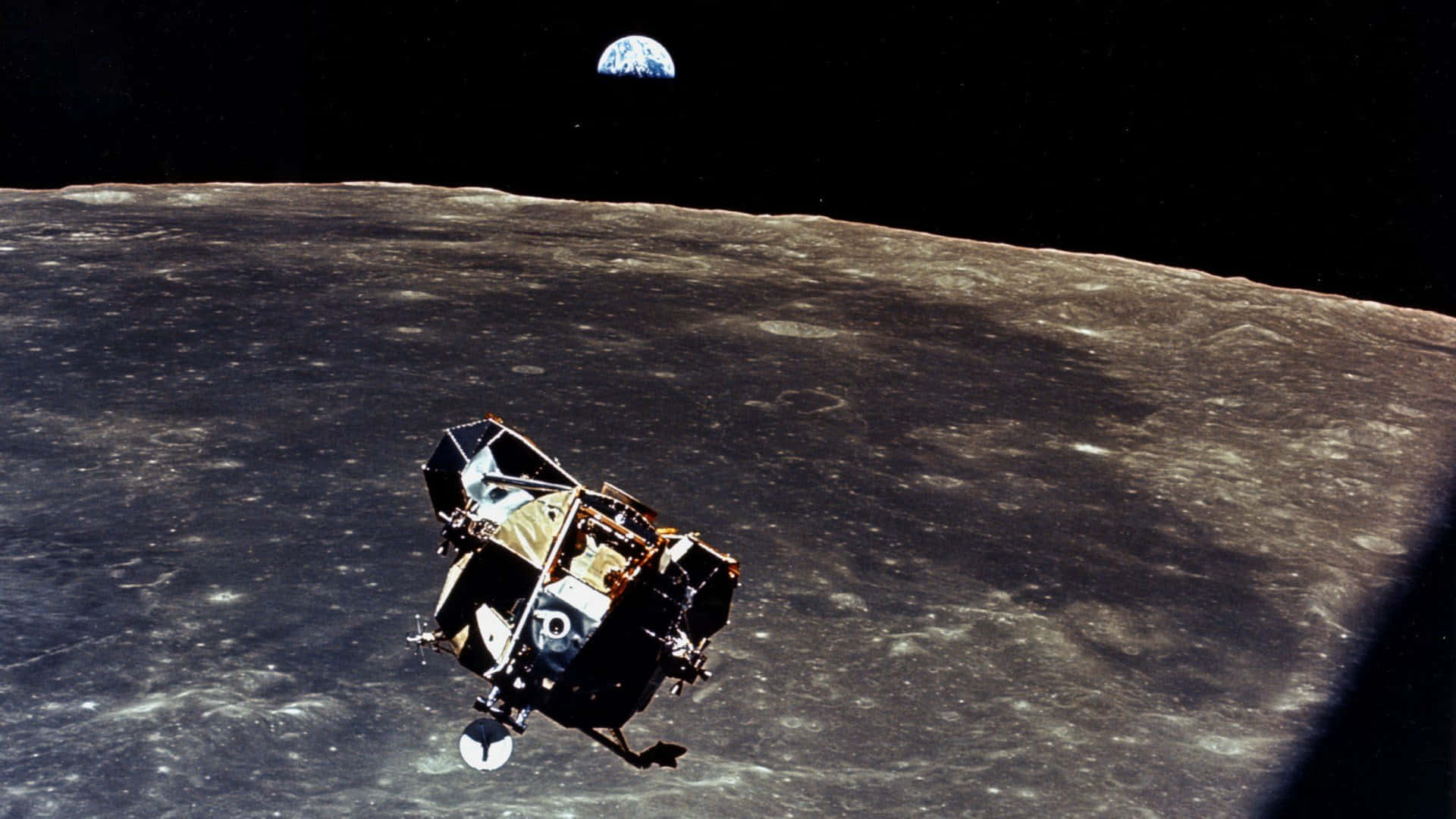 Space Mission 桌布 壁紙 — 一艘月球登陸器正降落到佈滿隕石坑的月球表面，地球在漆黑的太空中清晰可見。
