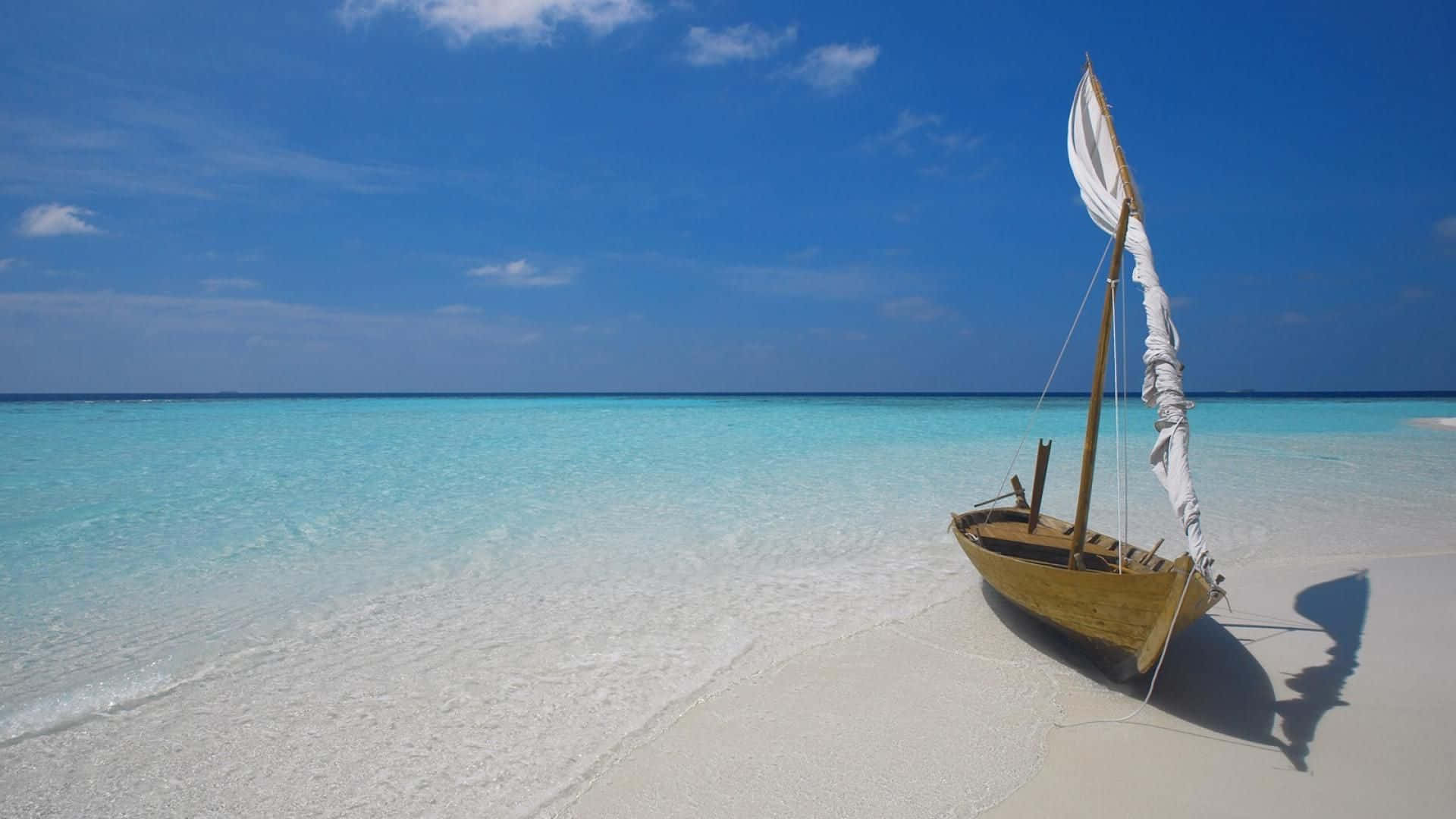 Maldives Beach 桌布 壁紙 — 一艘木製帆船停泊在清澈藍天下、碧綠海水旁的純白沙灘上。