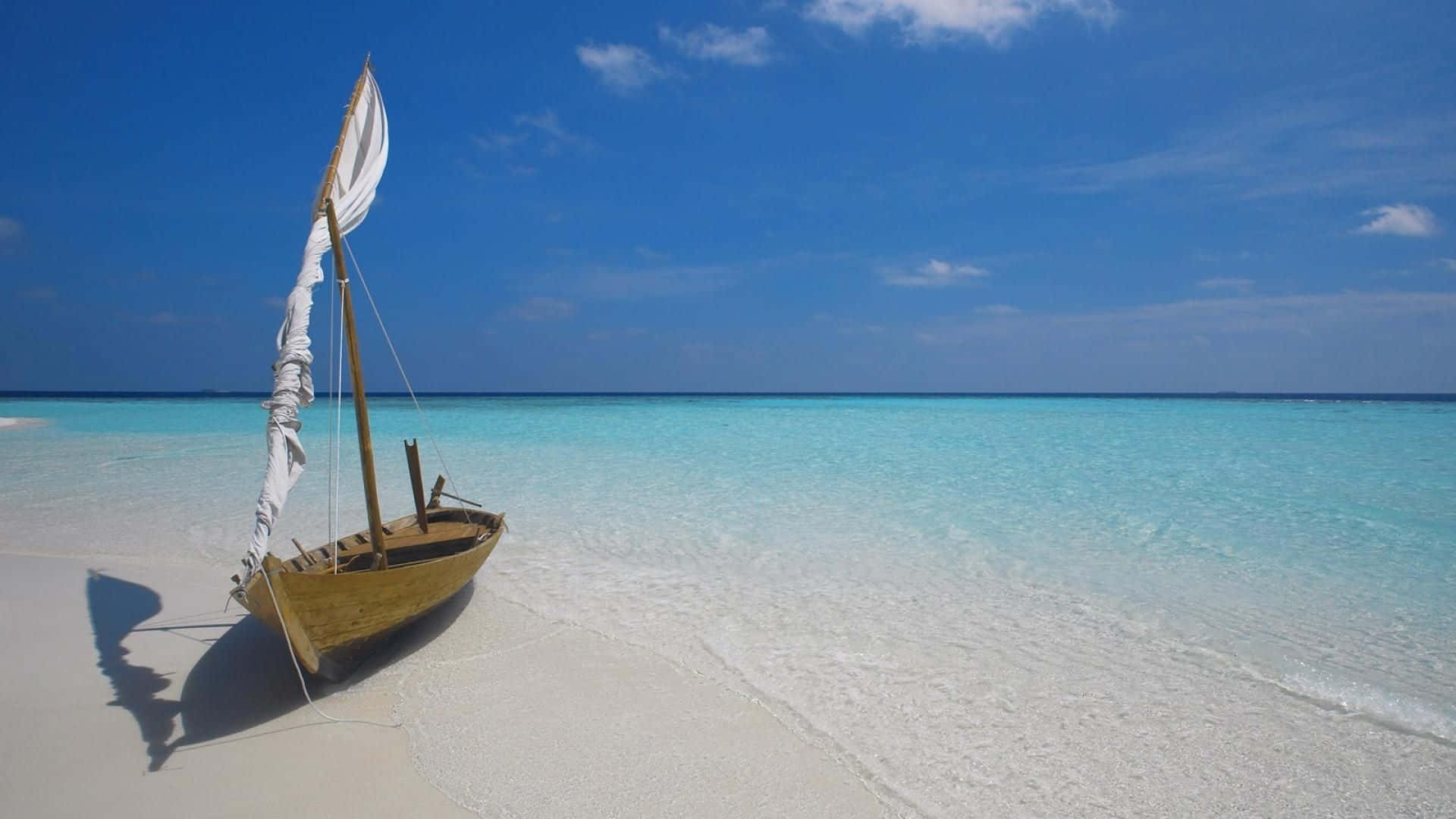 Maldives Beach 桌布 壁紙 — 一艘木製帆船停泊在清澈藍天下、碧綠海水旁的純白沙灘上。