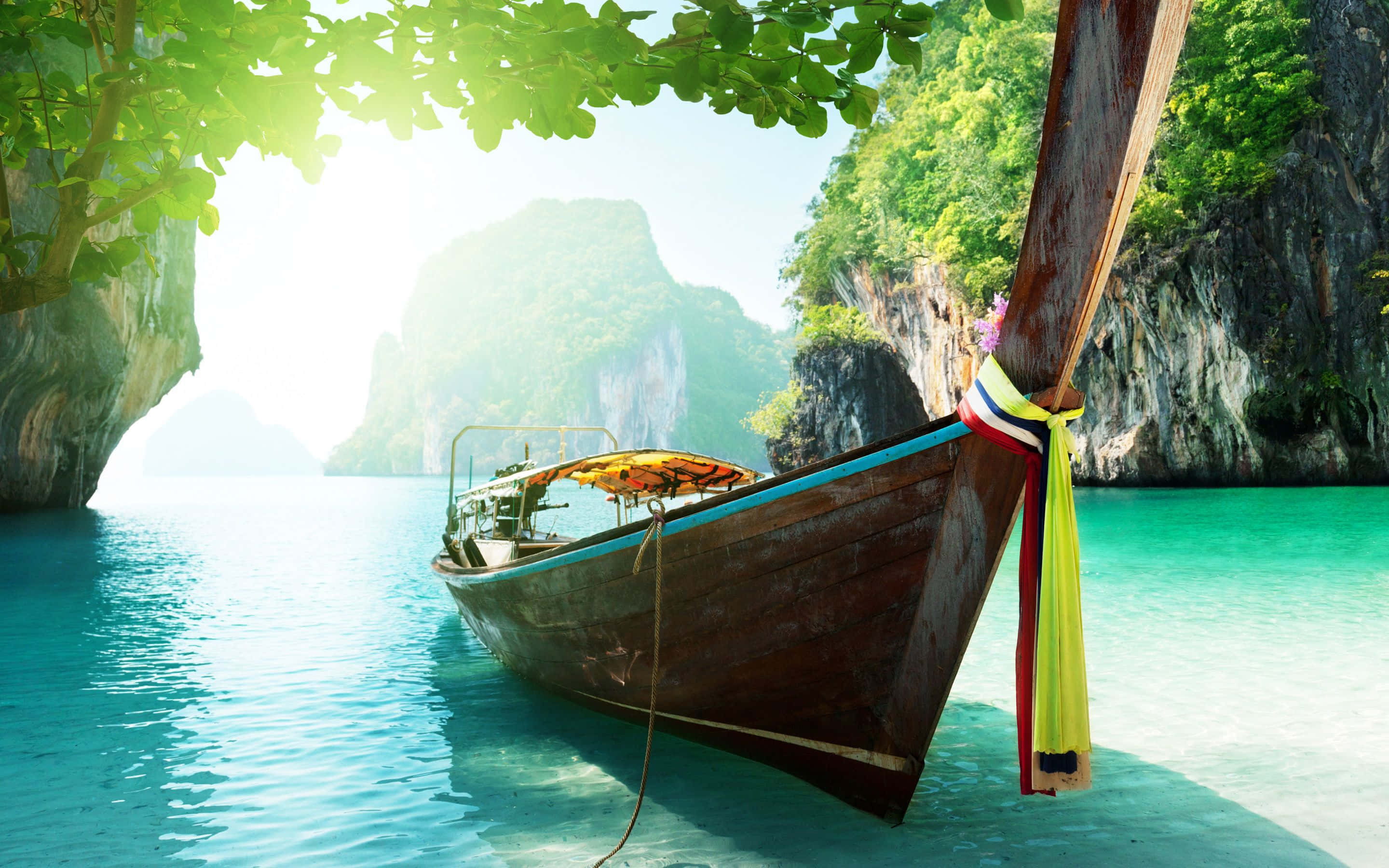 Thailand 桌布 壁紙 — 一艘木製長尾船停泊在晶瑩剔透的碧綠海水中，四周環繞著鬱鬱蔥蔥的綠色懸崖和斑駁的陽光。