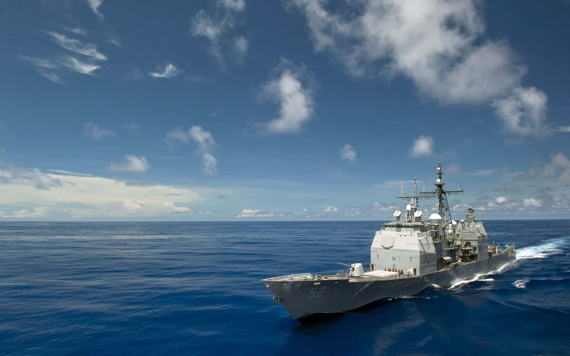 Navy 桌布 壁紙 — 一艘灰色海軍驅逐艦在晴朗的天空下，伴隨著散落的白色雲朵，劃過深藍色的海洋。