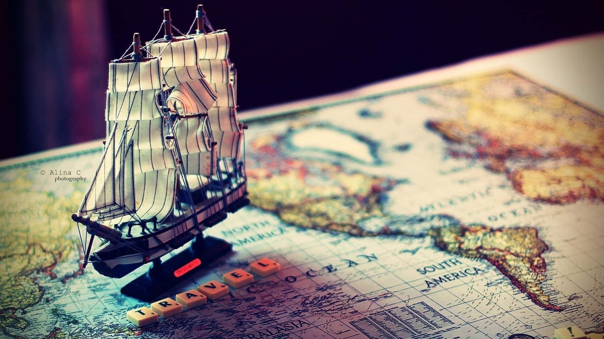 3d Travel 桌布 壁紙 — 一艘精細的模型船停放在一張古董世界地圖上，地圖上有木塊拼出的'TRAVEL'字樣。