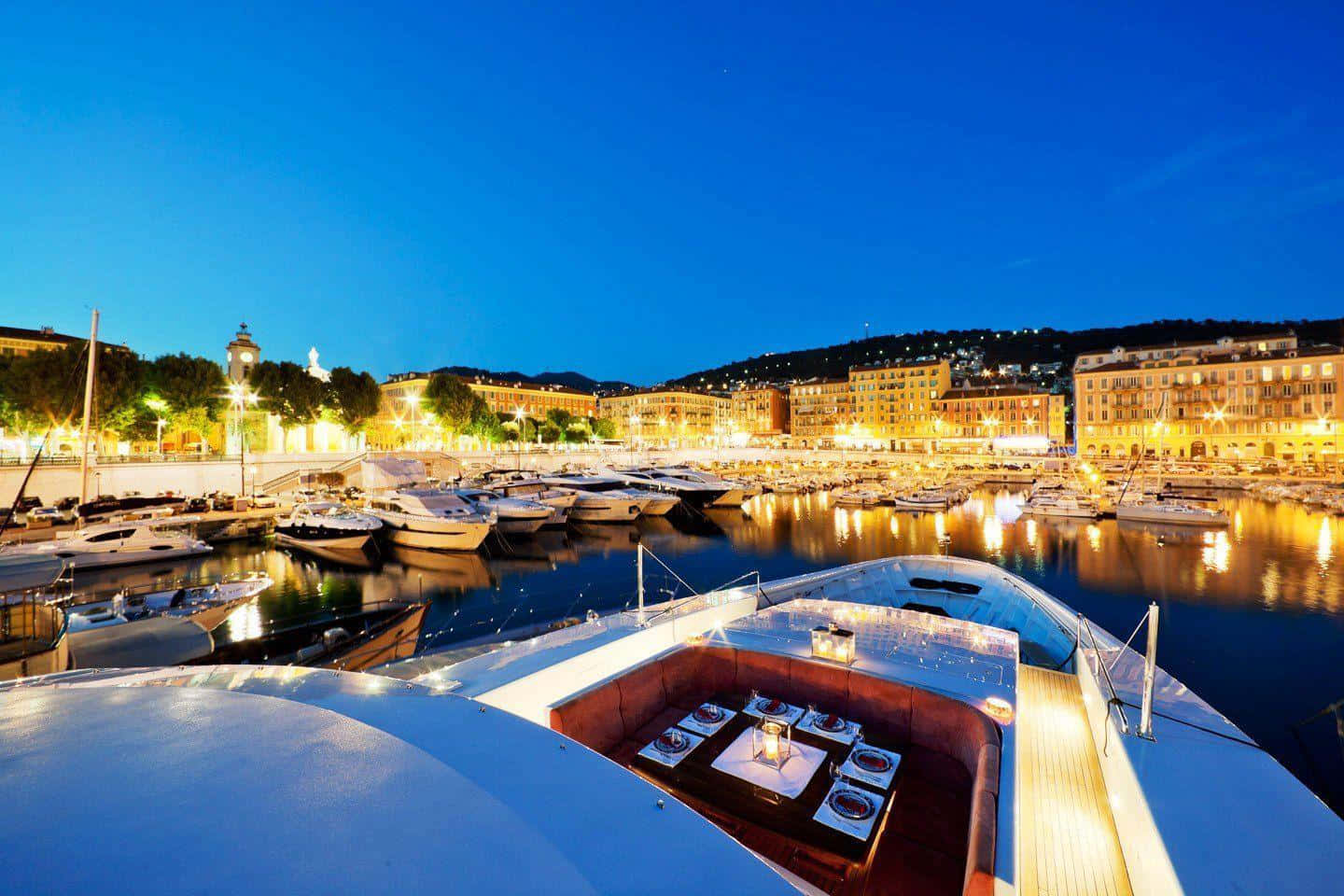 Yacht 桌布 壁紙 — 一艘豪華遊艇設有燈光照明嘅用餐區，俯瞰住深藍色暮色天空下停滿船隻嘅碼頭。