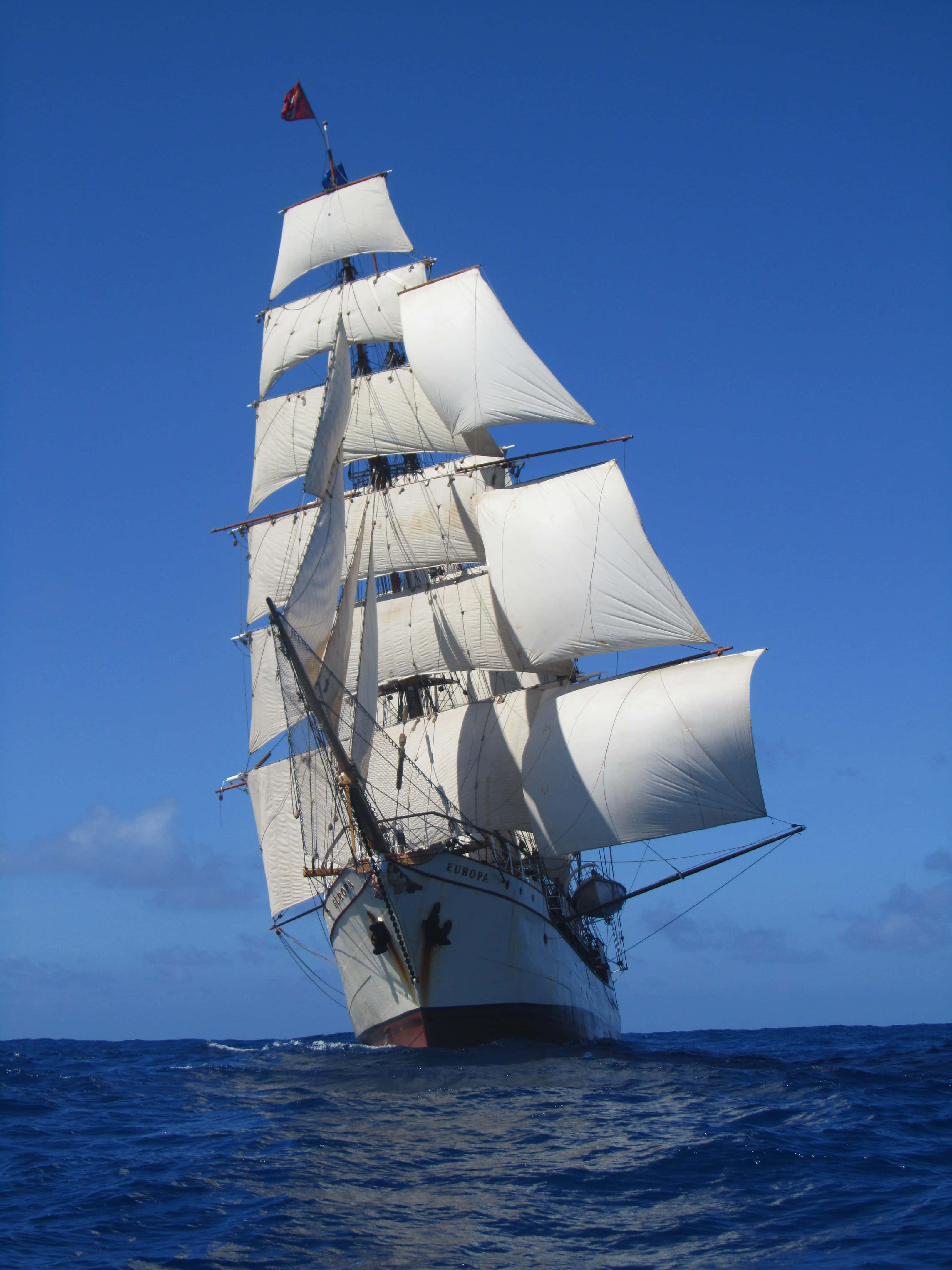 Ship 桌布 壁紙 — 一艘雄偉的高桅帆船，白色船帆迎風鼓脹，在清澈蔚藍的天空下劃過深藍色的海洋。