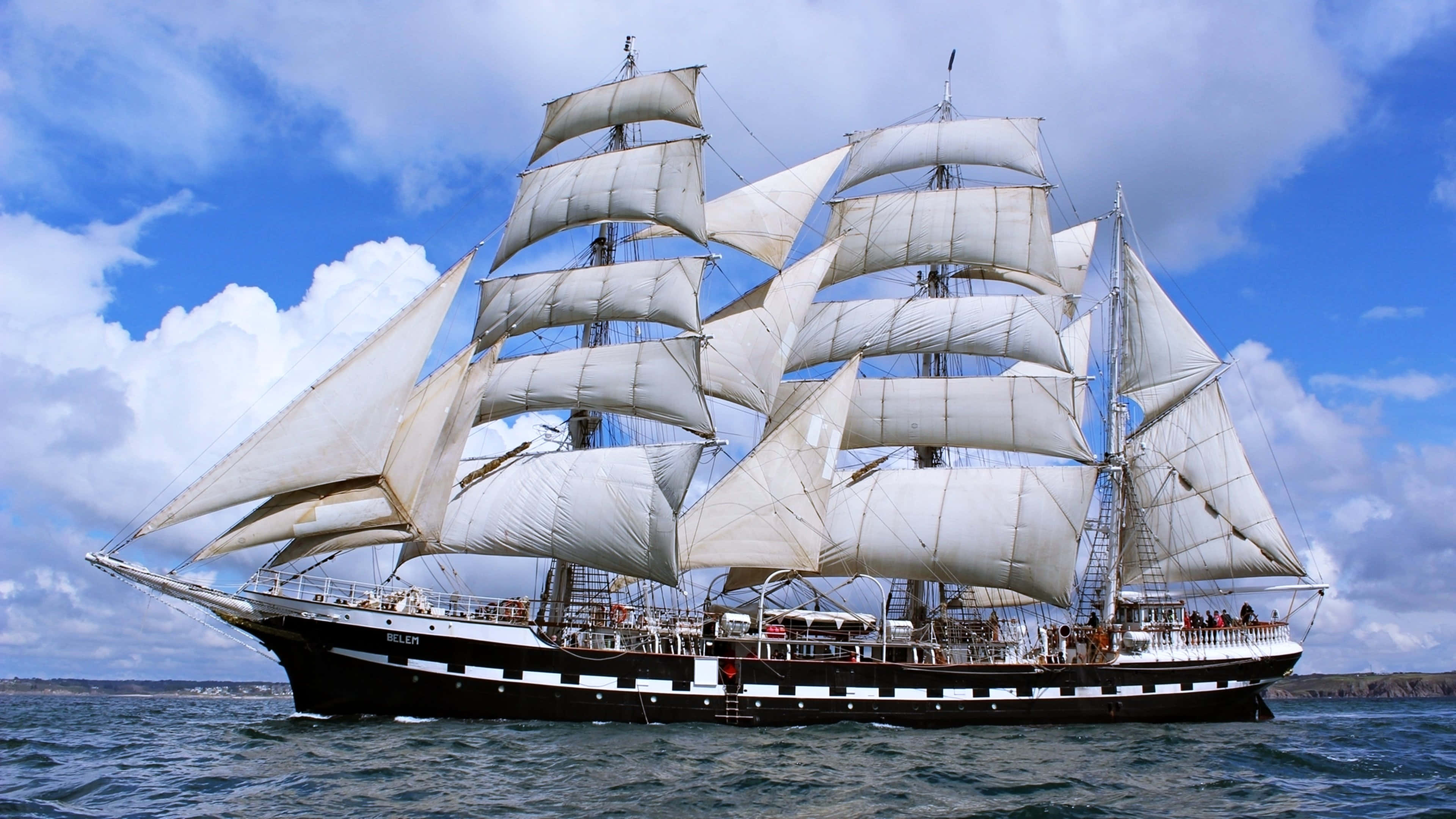 Ship 桌布 壁紙 — 一艘雄偉的高桅帆船，鼓滿白色風帆，在部分多雲的天空下，滑過深藍色的水域。