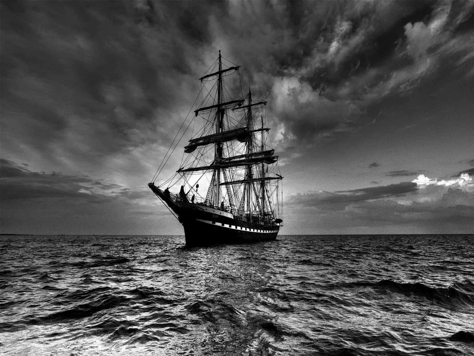 Black And White Ocean 桌布 壁紙 — 一艘雄偉的高桅帆船在波濤洶湧的海面上航行，天空烏雲密佈，呈現單色調的戲劇性效果。