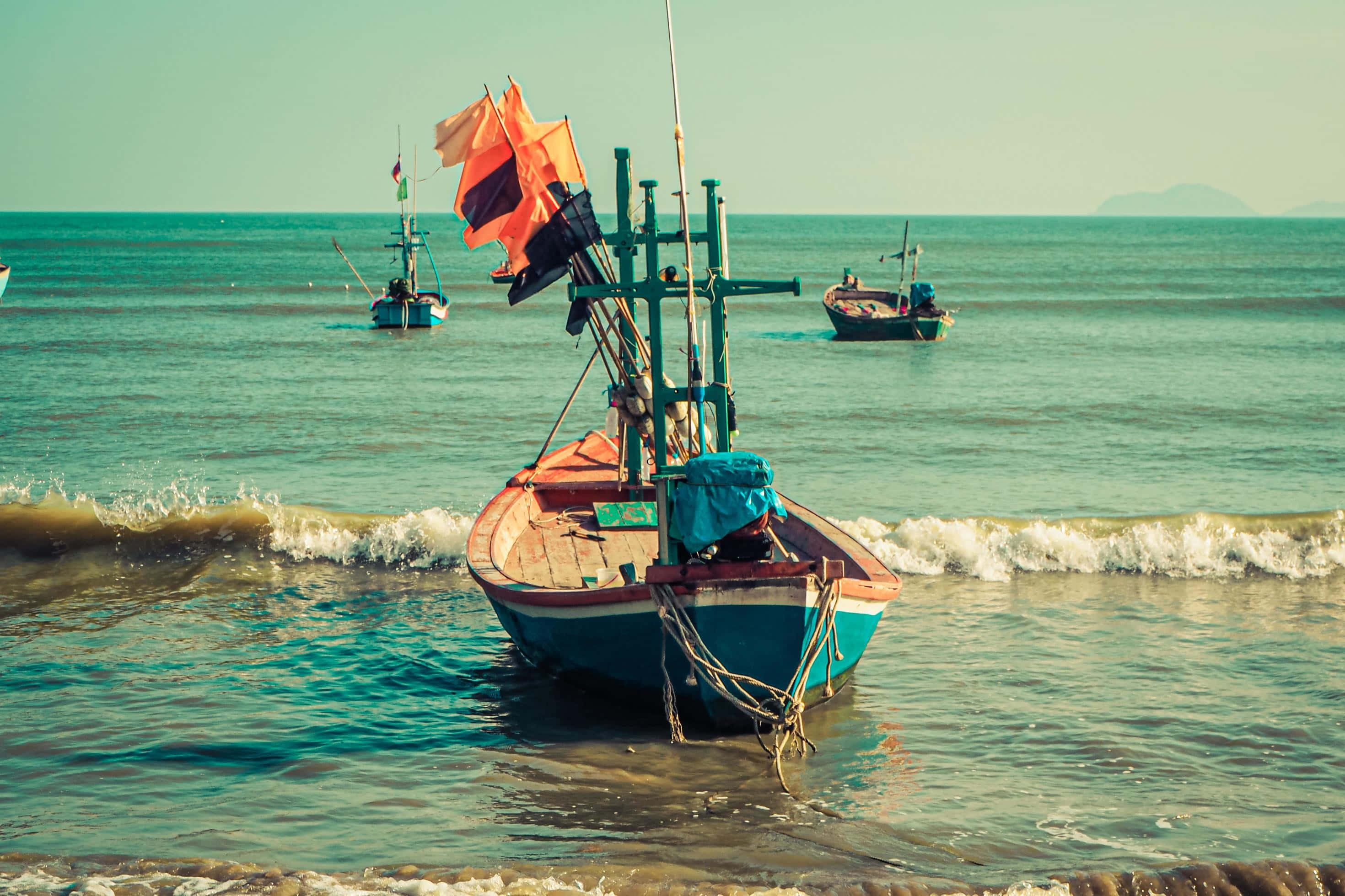 Boating 桌布 壁紙 — 一艘飽經風霜的漁船，掛著橙色帆，停泊在淺藍綠色的海水中，溫柔的海浪拍打著船身。