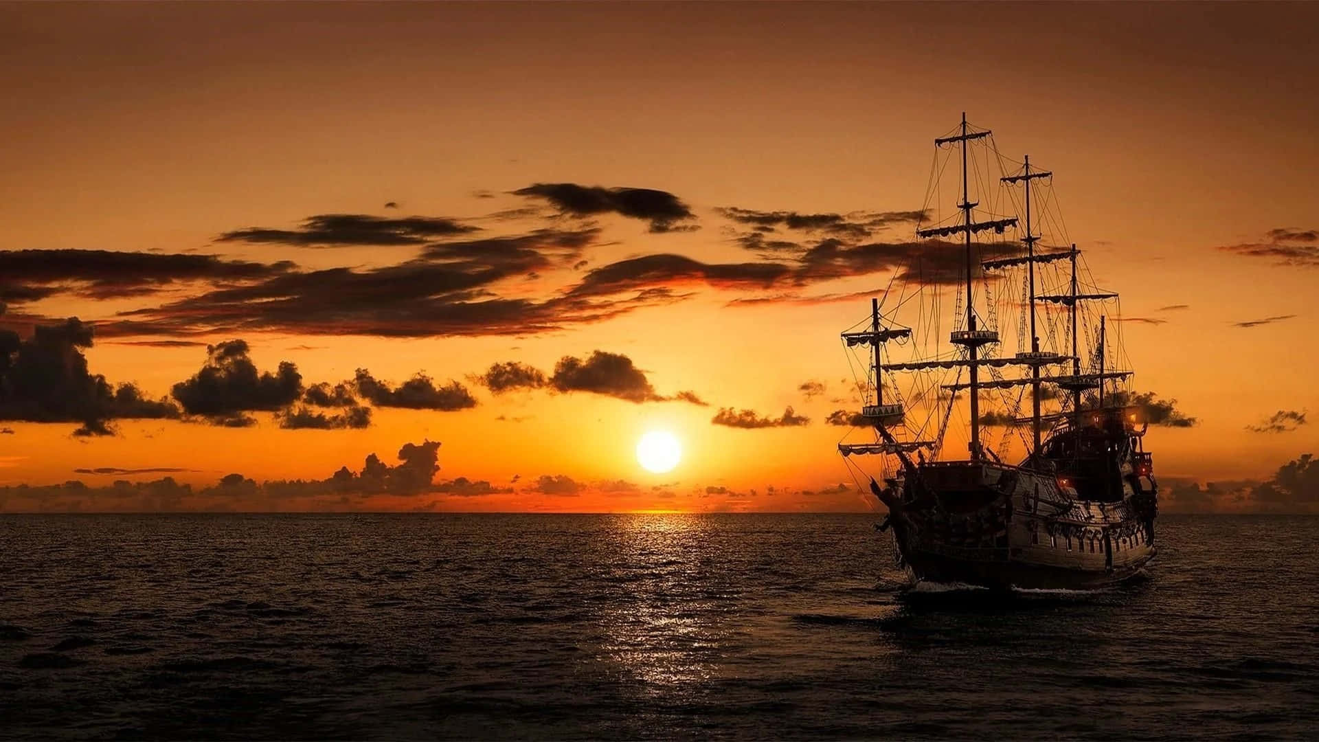 Ship 桌布 壁紙 — 一艘高大的帆船在平靜的海面上航行，夕陽在散落的雲層後方呈現出火熱的橙色和金色色調。
