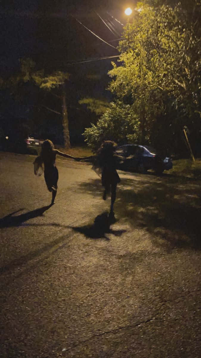 兩個小孩手牽手在夜晚黑暗的街道上，在街燈下奔跑。