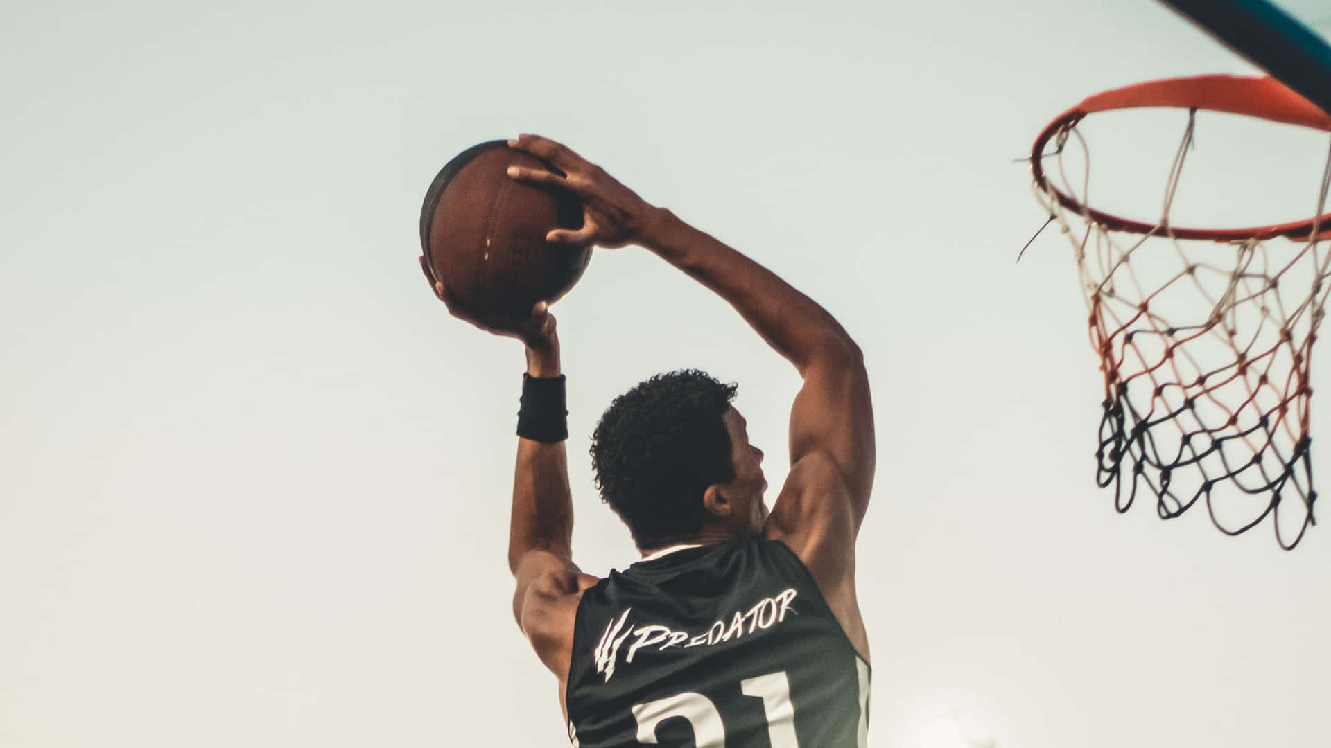 身穿綠色球衣的運動員在明亮天空下靠近籃框灌籃。
