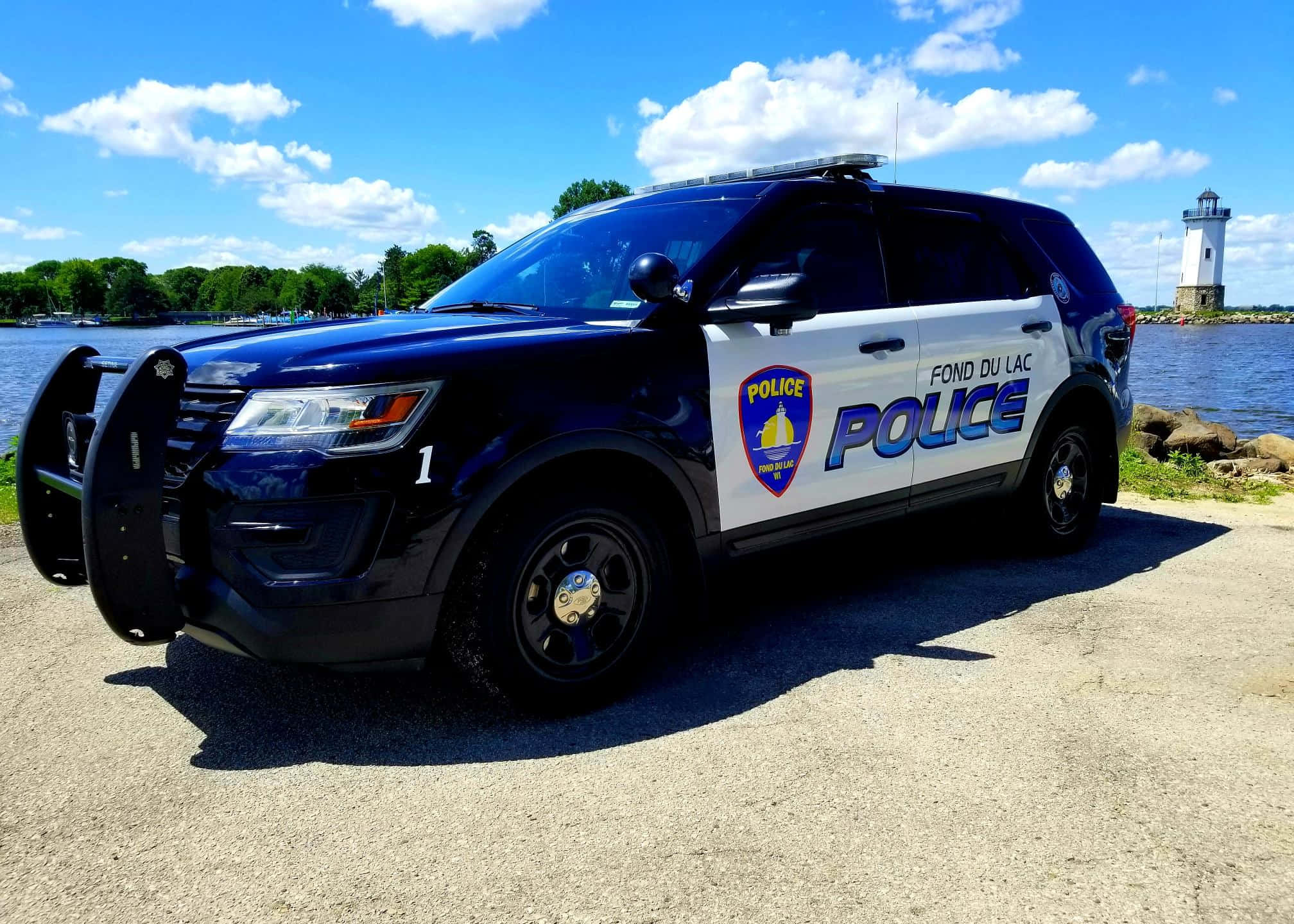 警察 桌布 壁紙 — 一輛 Fond du Lac 警用 SUV 停泊在陽光明媚的湖邊，背景有燈塔。