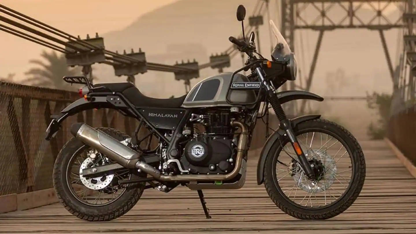 自行車 桌布 壁紙 — 一輛 Royal Enfield Himalayan 電單車在朦朧的金色天空下，以遠處的山脈和纜車設施為背景，佇立在木橋上。
