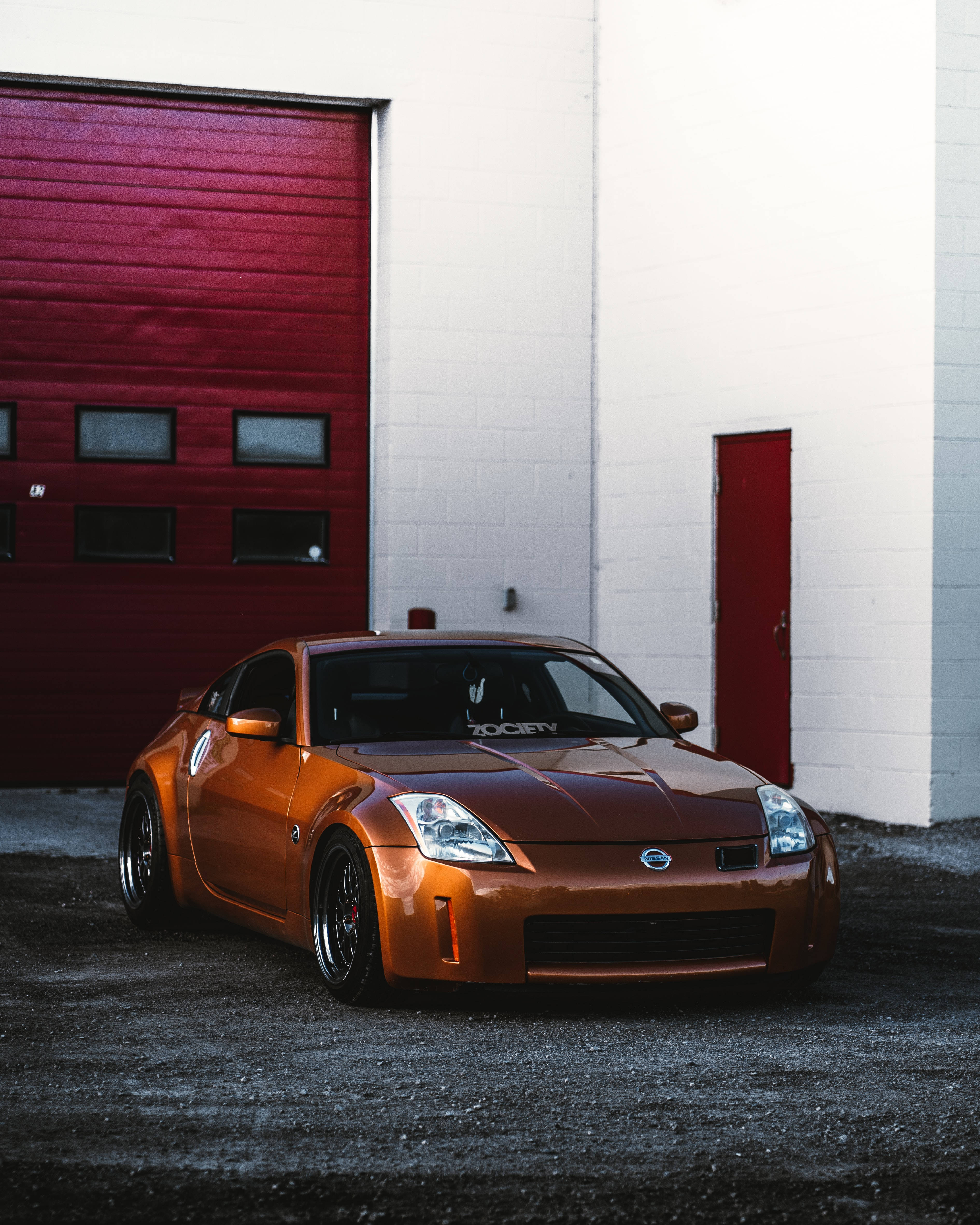 Nissan 350Z 壁紙 — 一輛亮橙色的日產350Z跑車停在一棟白色建築物前，建築物有紅色車庫門和紅色門。