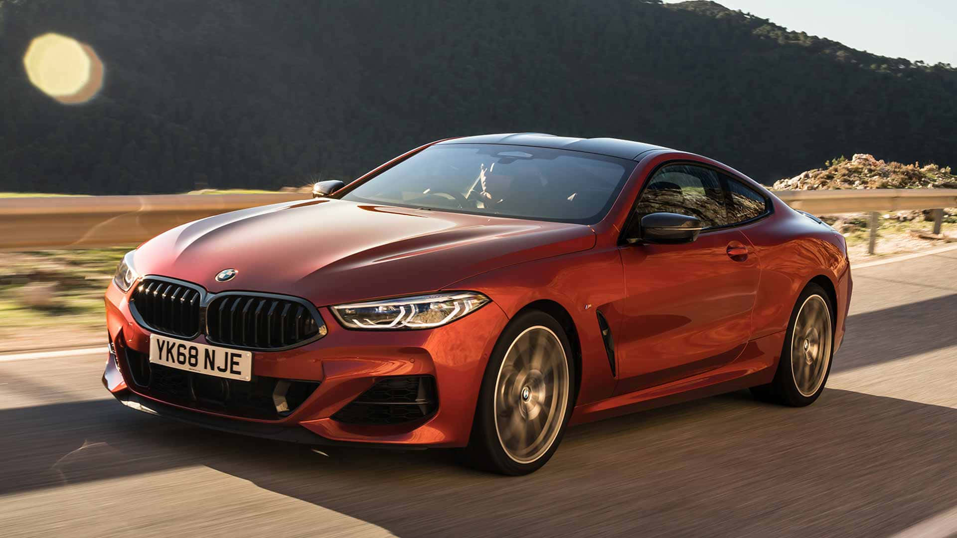 Bmw 8 Series 桌布 壁紙 — 一輛亮紅色BMW 8系雙門轎跑車在明亮的陽光下沿著蜿蜒的山路疾馳。