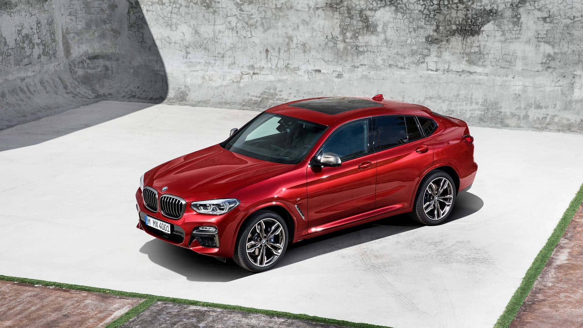Bmw X4 桌布 壁紙 — 一輛亮紅色BMW X4 SUV停在混凝土平台上，背景是風化灰色牆壁，在明亮的日光下。
