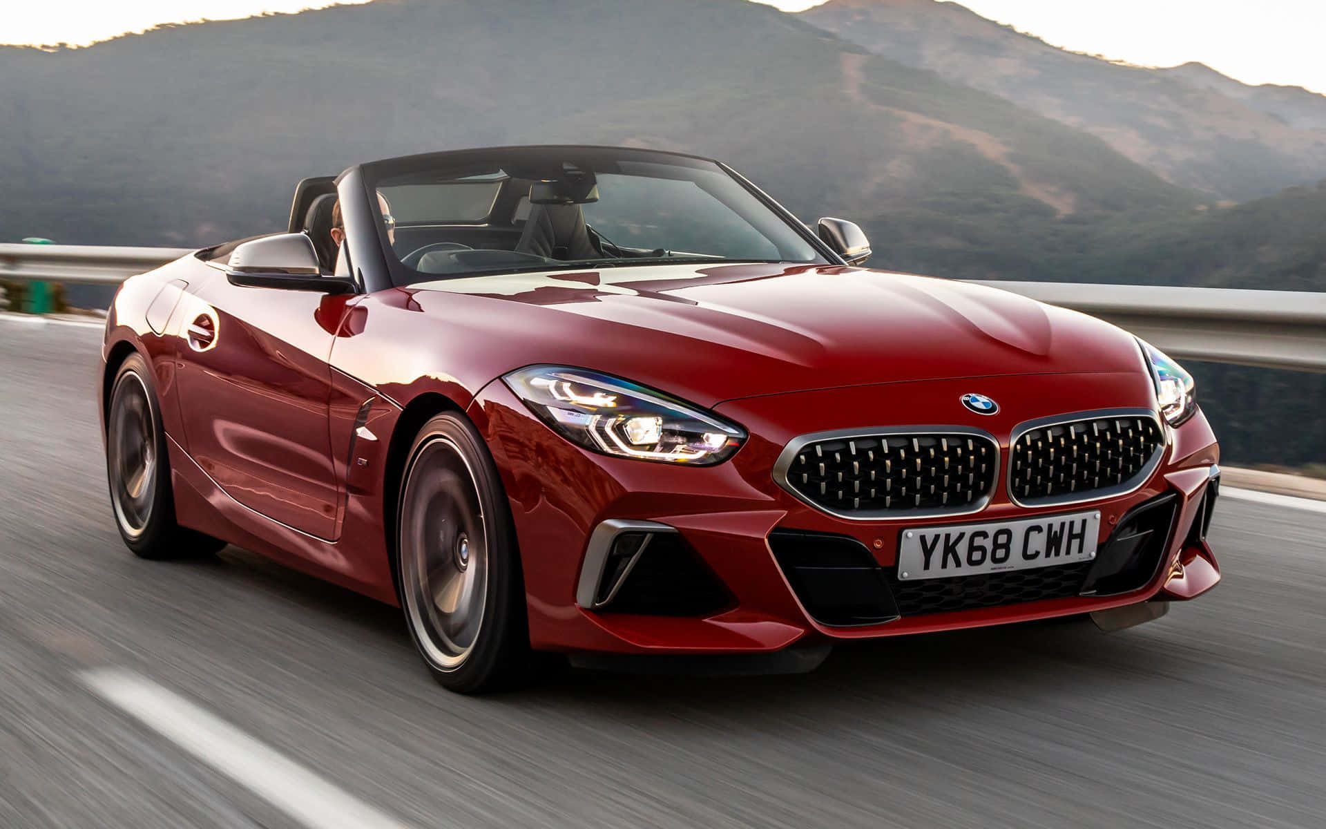 Bmw Z4 桌布 壁紙 — 一輛亮紅色BMW Z4開篷跑車在高速公路上飛馳，背景是模糊的動態和陽光照耀的山丘。