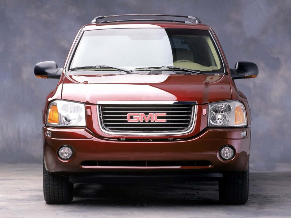 Gmc Envoy 桌布 壁紙 — 一輛亮紅色GMC SUV正面朝向帶有紋理的灰色工作室背景，搭配戲劇性燈光。