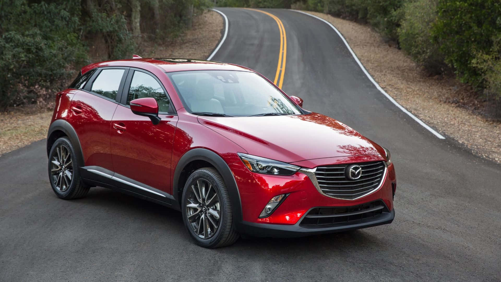 Mazda Cx-3 桌布 壁紙 — 一輛亮紅色Mazda CX-3 SUV沿著蜿蜒的森林道路行駛，兩旁是茂密的綠樹。