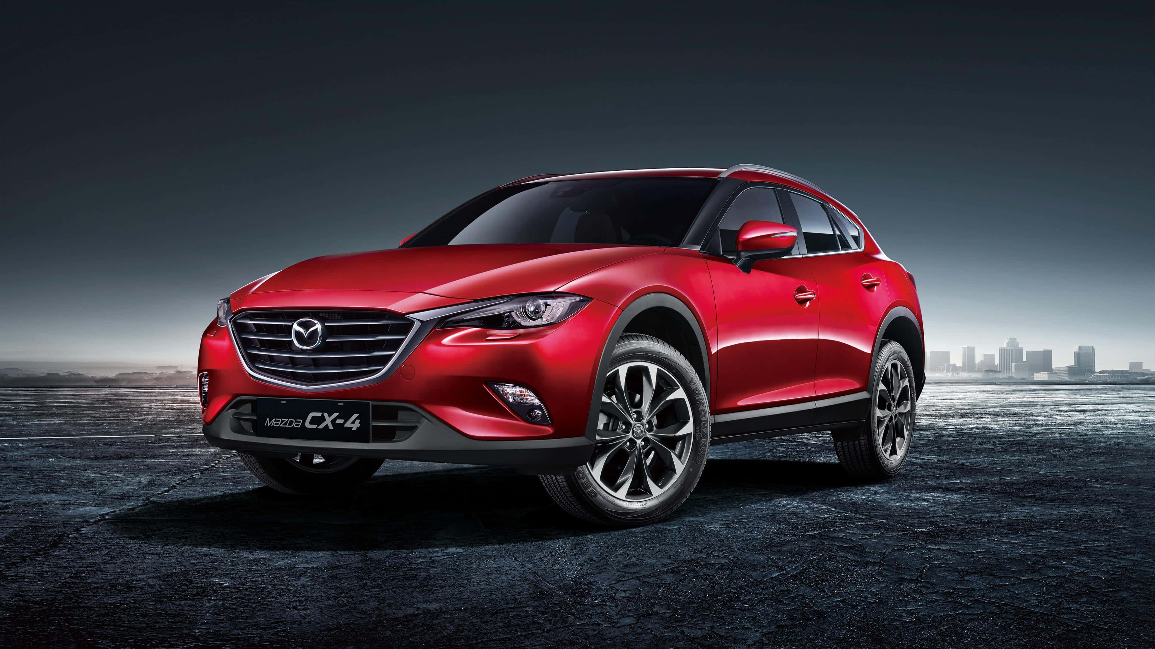 Mazda Cx-5 桌布 壁紙 — 一輛亮紅色Mazda CX-4 SUV停在濕漉漉的瀝青路面上，背景是朦朧的城市天際線，籠罩在陰鬱的暮色天空下。