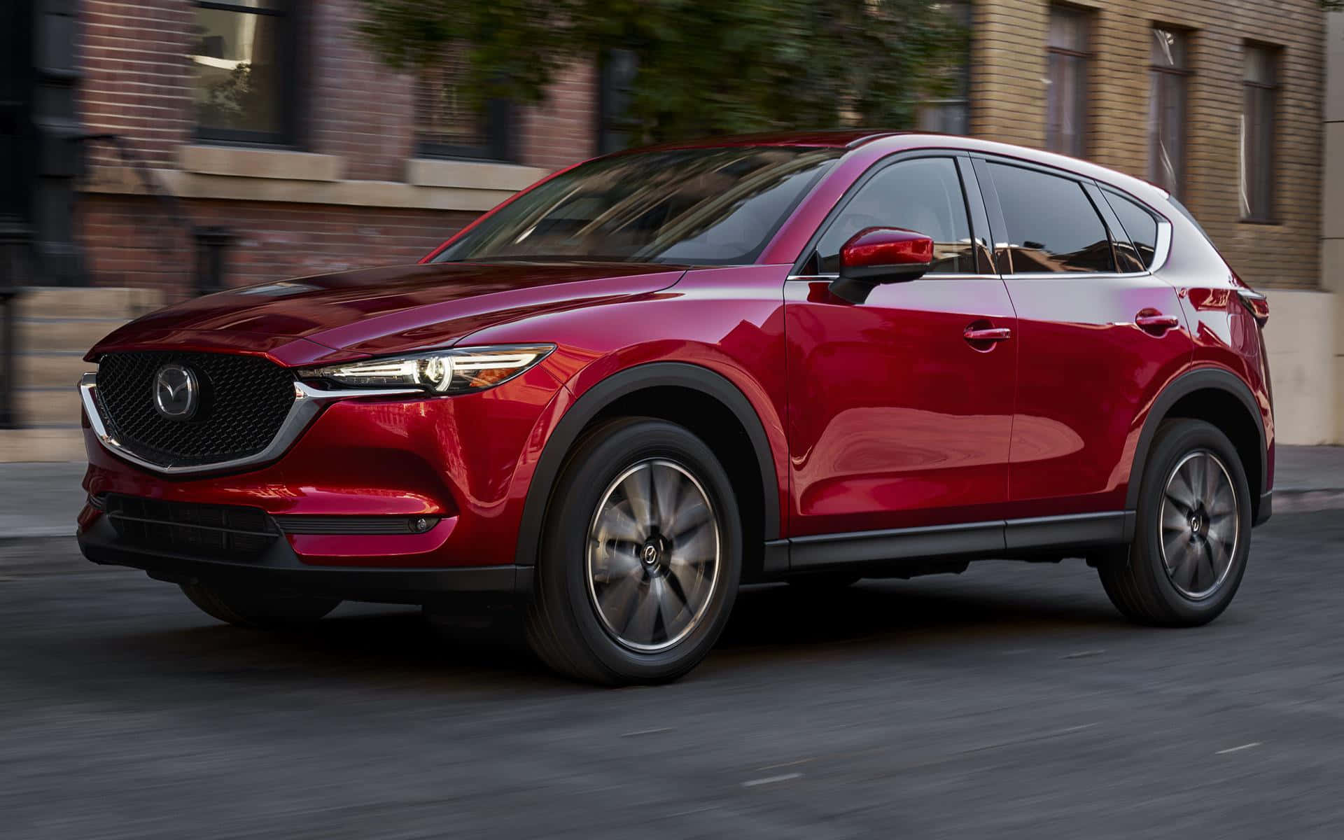 Mazda Cx-5 桌布 壁紙 — 一輛亮紅色Mazda CX-5 SUV在磚砌建築和動態模糊背景的城市街道上行駛。