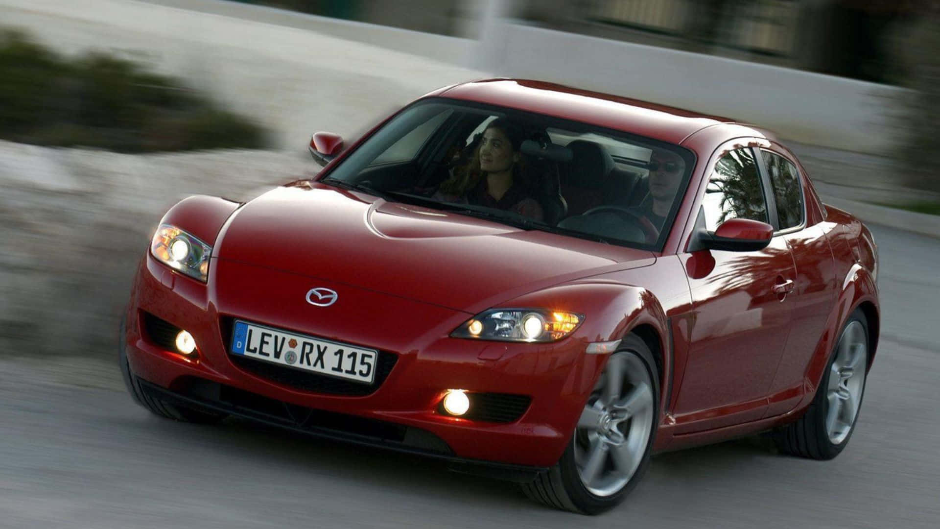 Mazda Rx-8 桌布 壁紙 — 一輛亮紅色Mazda RX-8跑車在模糊的道路上飛馳，車內可見兩名乘客。