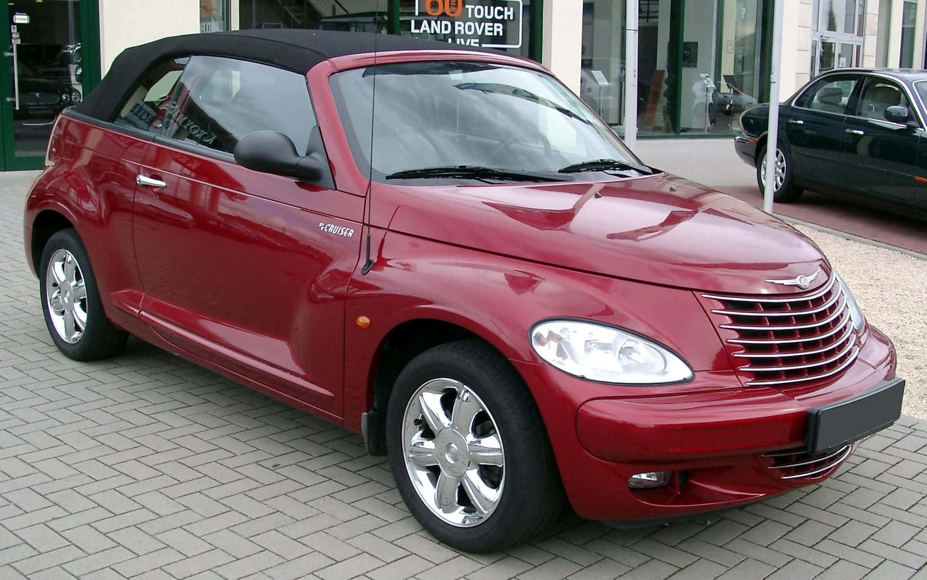 Chrysler Pt Cruiser 桌布 壁紙 — 一輛亮紅色PT Cruiser開篷車停泊在鋪砌的停車場上，背景有Land Rover經銷商。