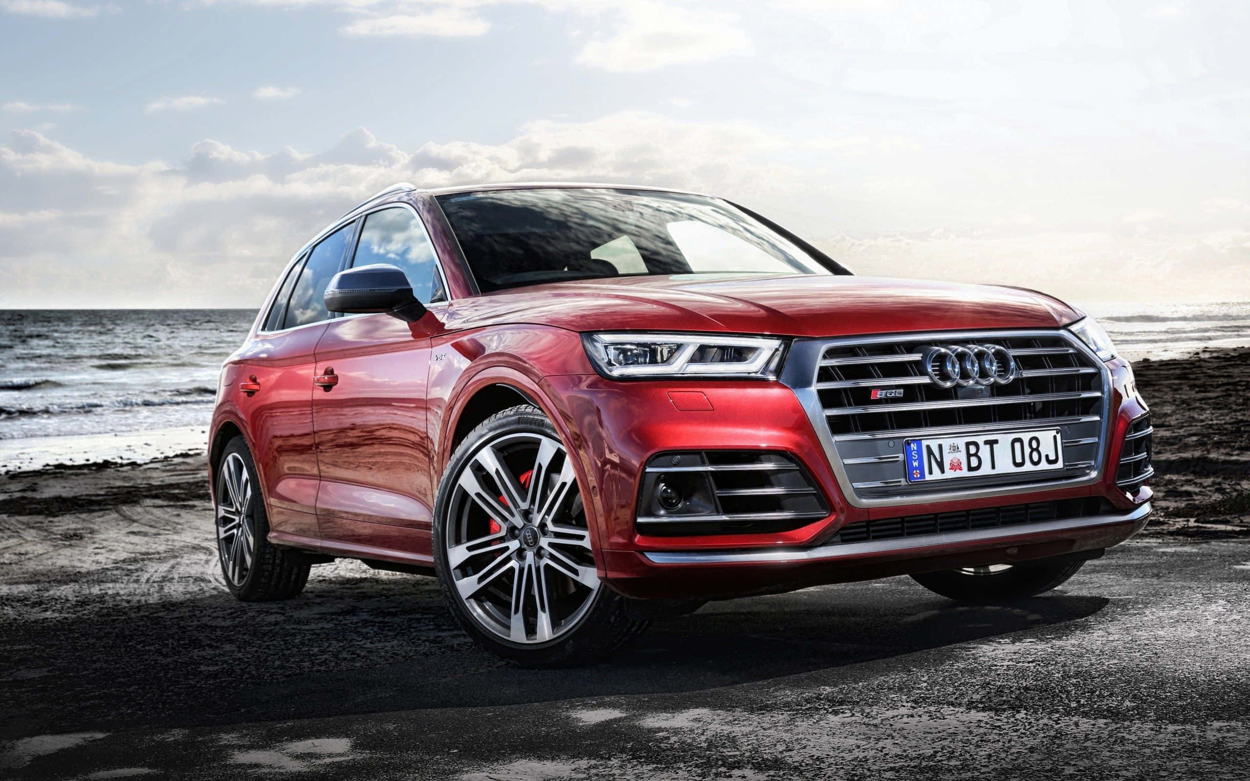 Audi Sq5 桌布 壁紙 — 一輛亮紅色奧迪SQ5 SUV停泊在濕漉漉的海灘上，背景是海浪和陰天。