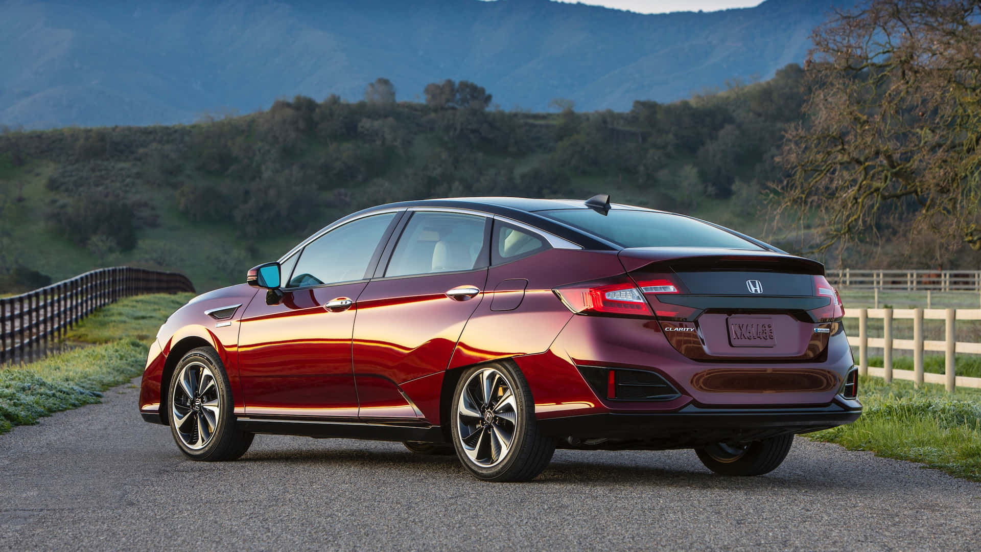 Honda Clarity 桌布 壁紙 — 一輛亮紅色本田Clarity插電式混合動力轎車停在碎石路上，背景有起伏的山丘和木柵欄。