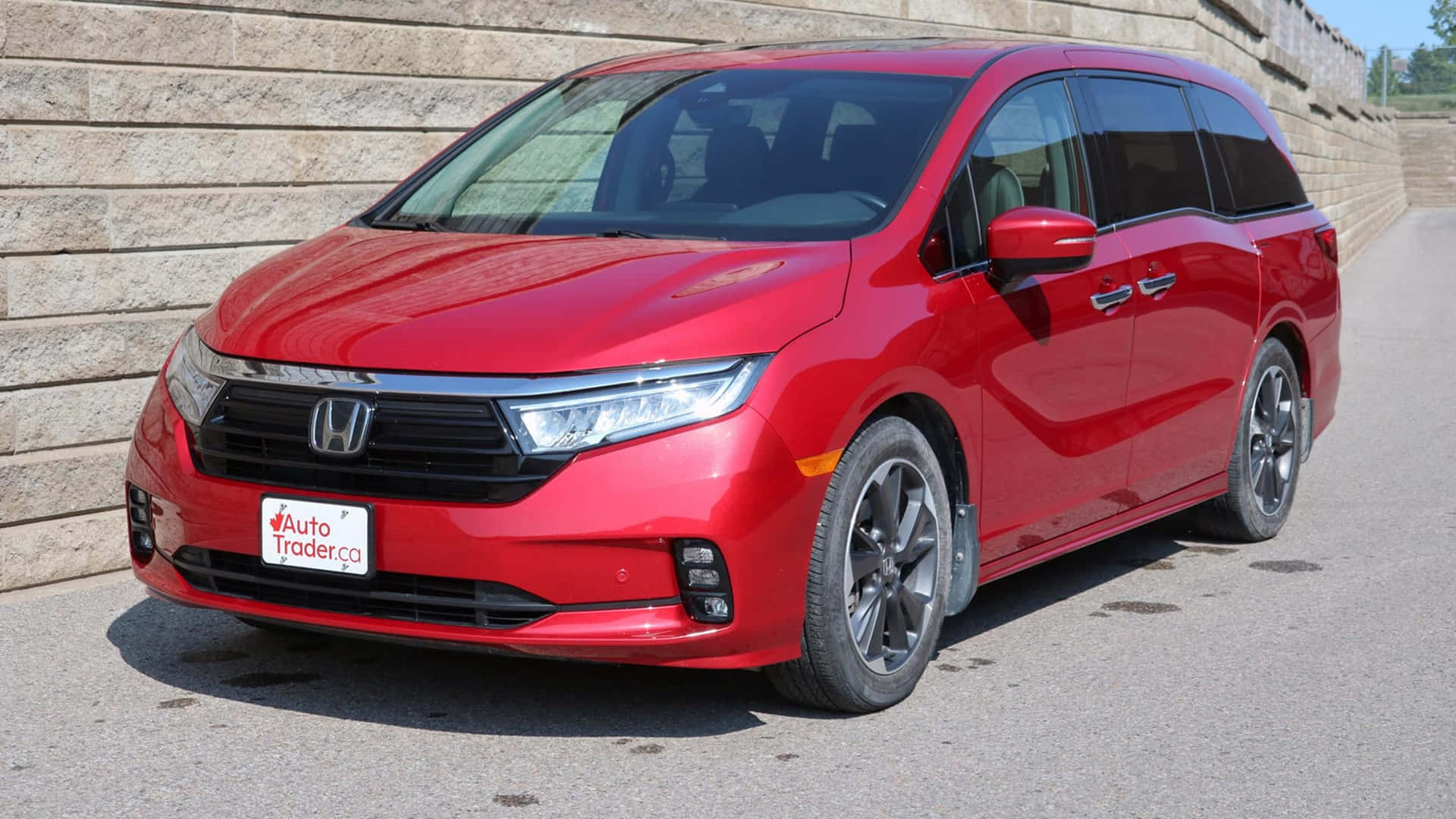 Honda Odyssey 桌布 壁紙 — 一輛亮紅色本田Odyssey小型貨車停在瀝青路上，旁邊是石牆，在明亮的日光下。