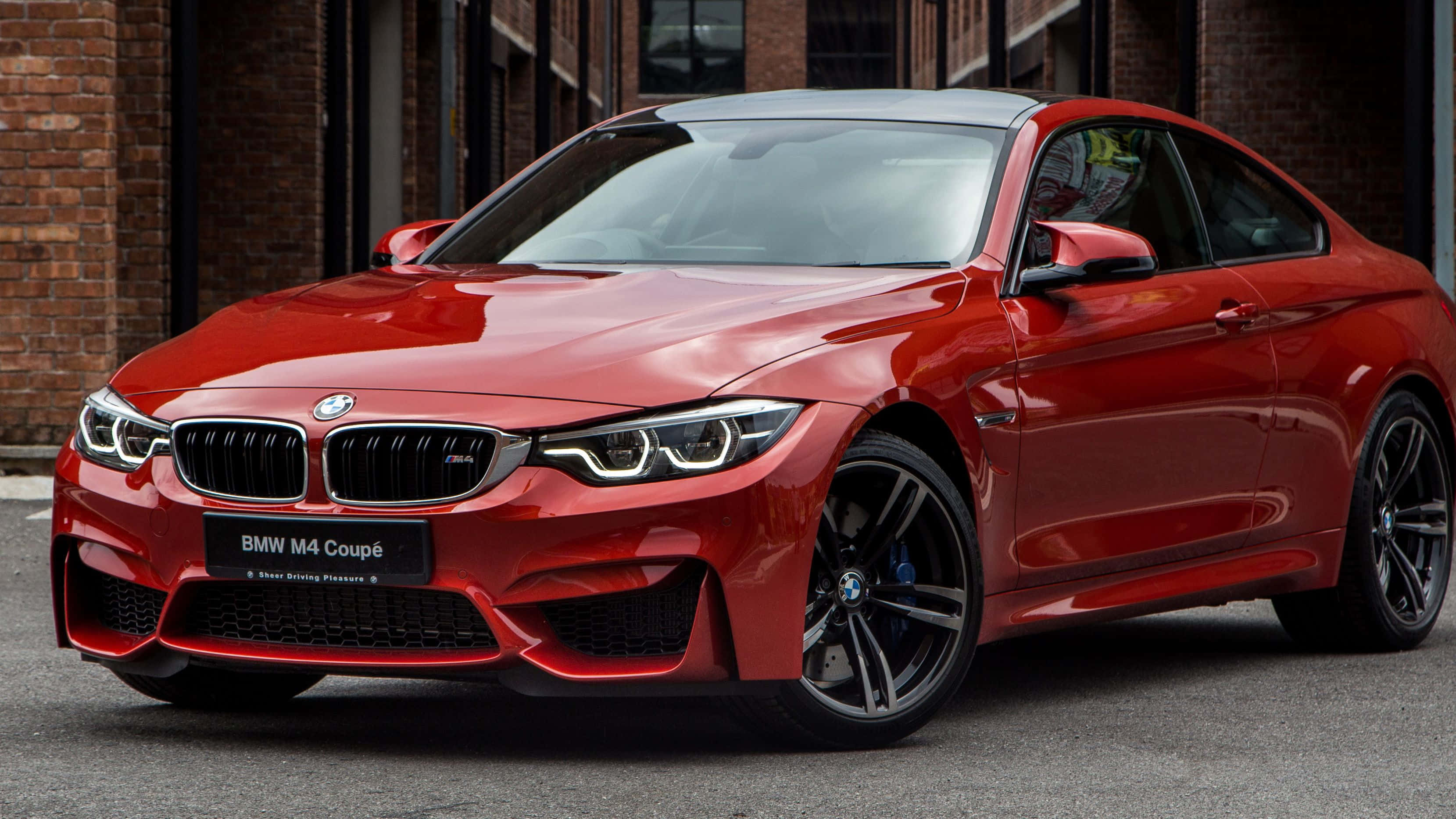 Bmw 4 Series 桌布 壁紙 — 一輛亮紅色的BMW M4 Coupe停在磚砌建築前，拋光表面上有銳利的反射。