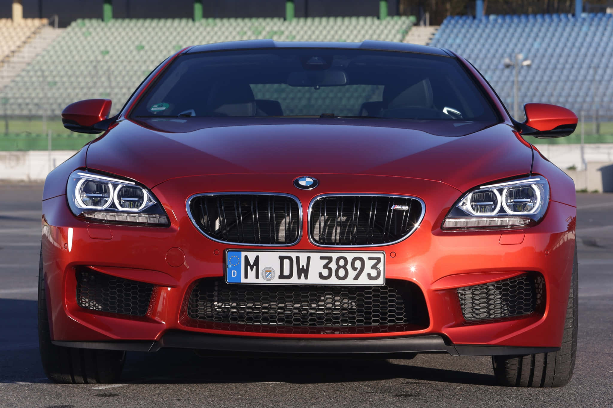 Bmw M6 桌布 壁紙 — 一輛亮紅色的BMW M6跑車在空曠的賽道上正面朝前，背景是體育場座位。