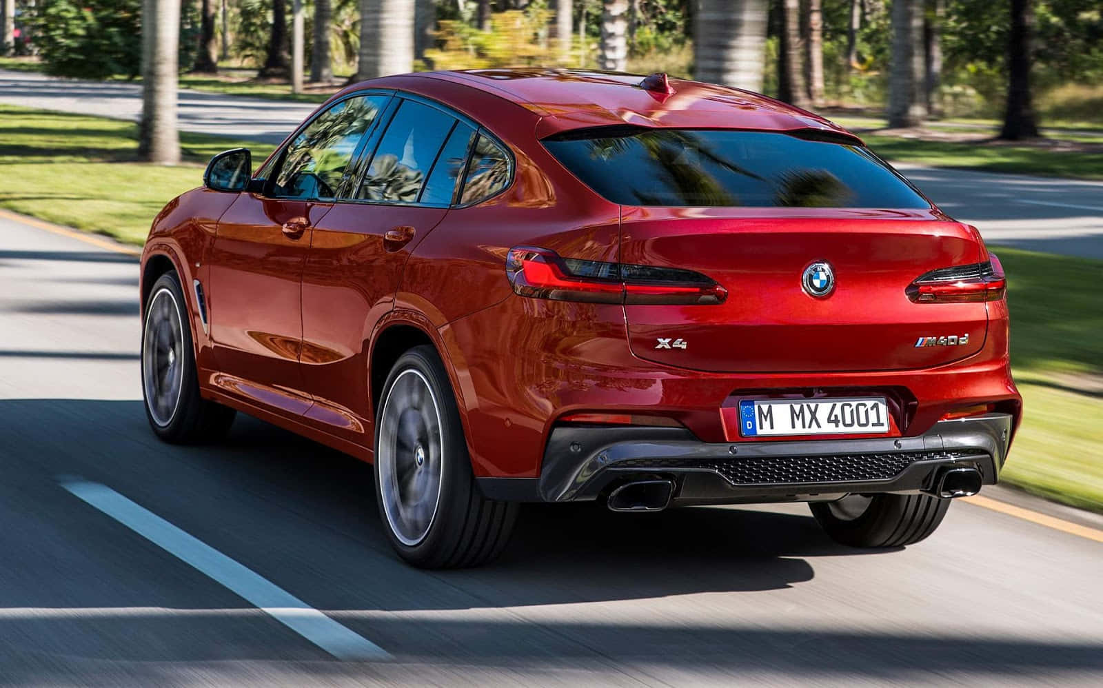 Bmw X4 桌布 壁紙 — 一輛亮紅色的BMW X4 M40i SUV在陽光明媚的林蔭大道上行駛，車輪帶有動態模糊效果。