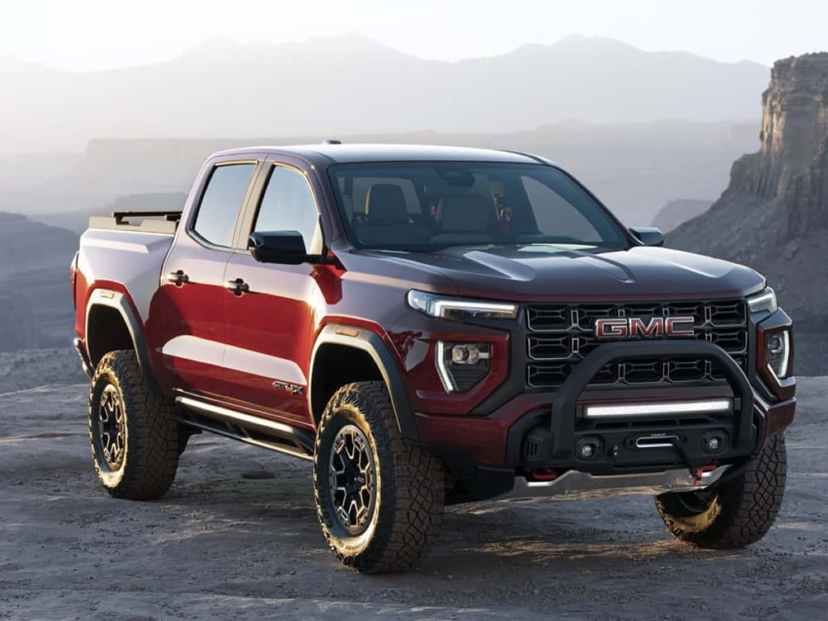 Gmc Canyon 桌布 壁紙 — 一輛亮紅色的GMC Canyon AT4皮卡車矗立在崎嶇的沙漠地形上，遠山在朦朧的天空下若隱若現。
