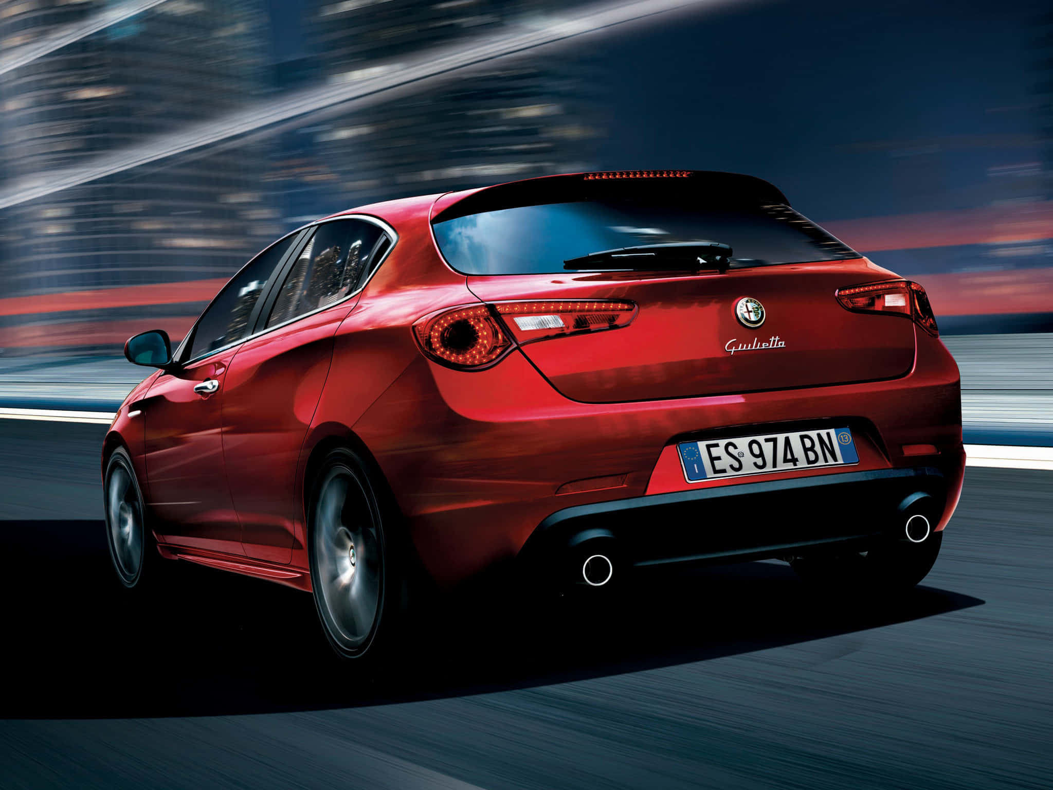 Alfa Romeo Giulietta 桌布 壁紙 — 一輛亮紅色的愛快羅密歐Giulietta在黃昏時分沿著模糊的高速公路飛馳，背景是流動的城市燈光。