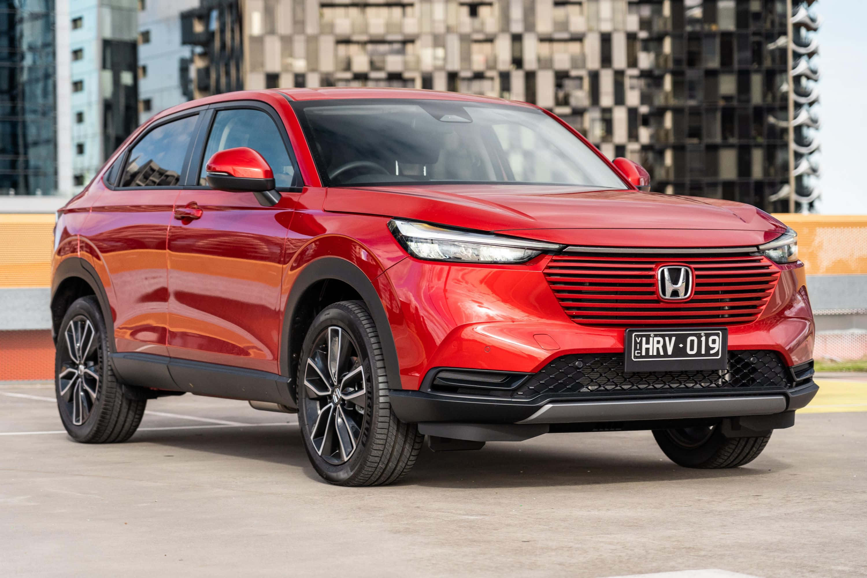 Honda Hr-v 桌布 壁紙 — 一輛亮紅色的本田HR-V SUV停放在現代都市環境中，背景是玻璃建築。