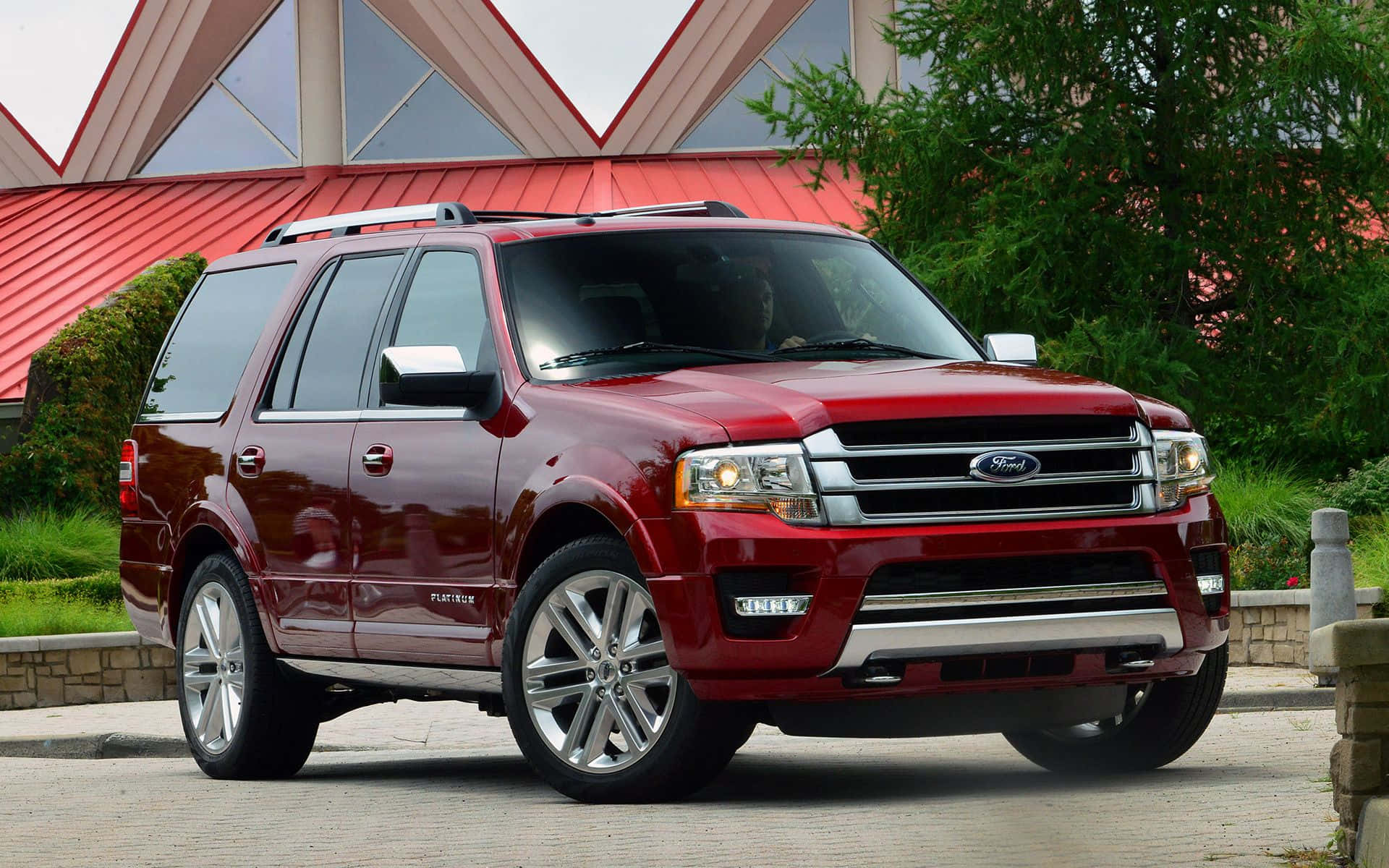 Ford Expedition 桌布 壁紙 — 一輛亮紅色的福特 Expedition SUV 停泊在石頭車道上，背景有現代建築和綠化。