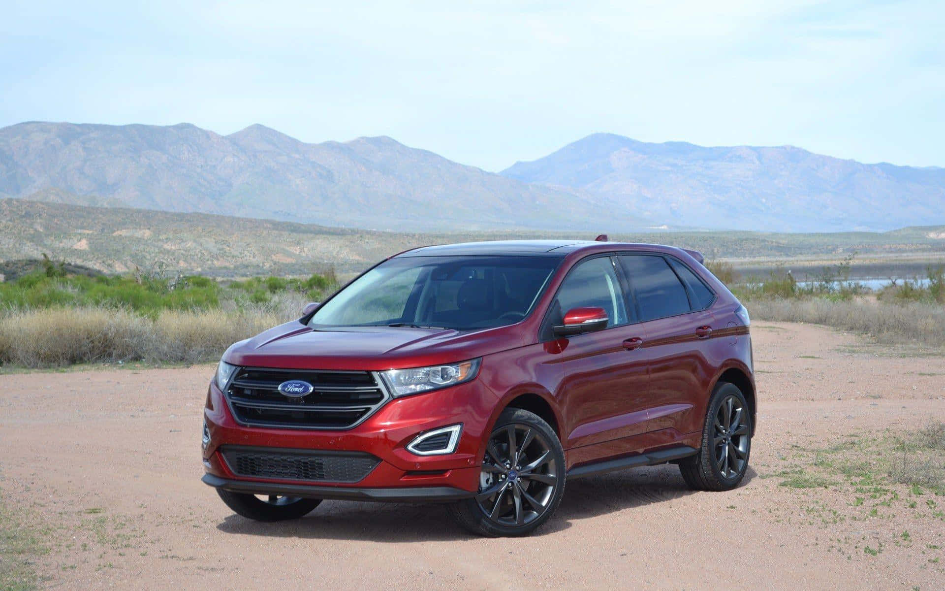 Ford Edge 桌布 壁紙 — 一輛亮紅色的福特Edge SUV停泊在塵土飛揚的小路上，遠處有山脈和乾草，天空明亮。