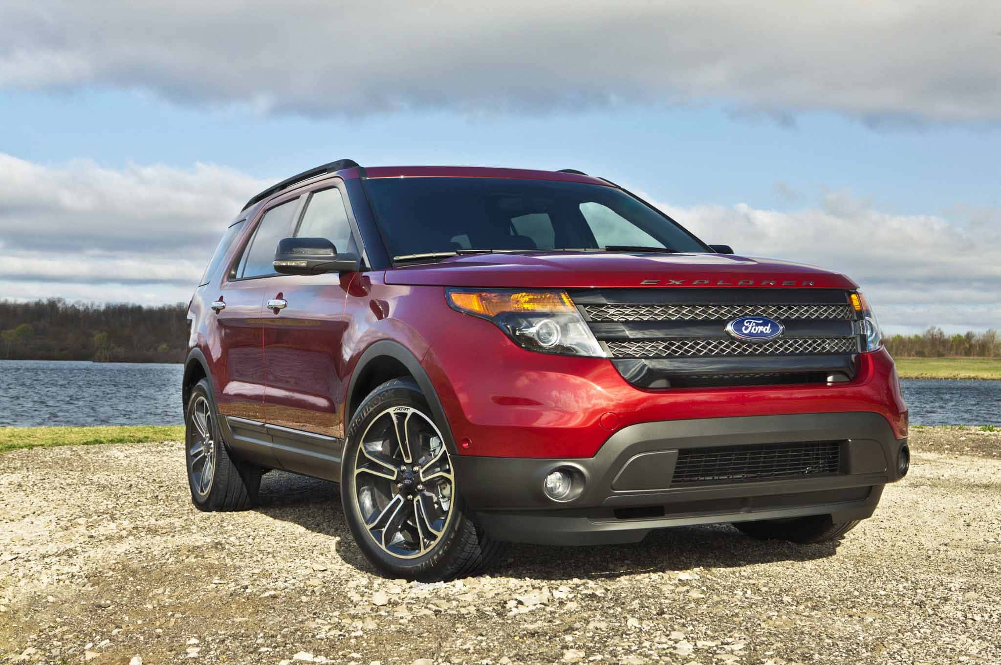 Ford Explorer 桌布 壁紙 — 一輛亮紅色的福特探險者SUV停在碎石路上，旁邊是平靜的湖泊，天空部分多雲。