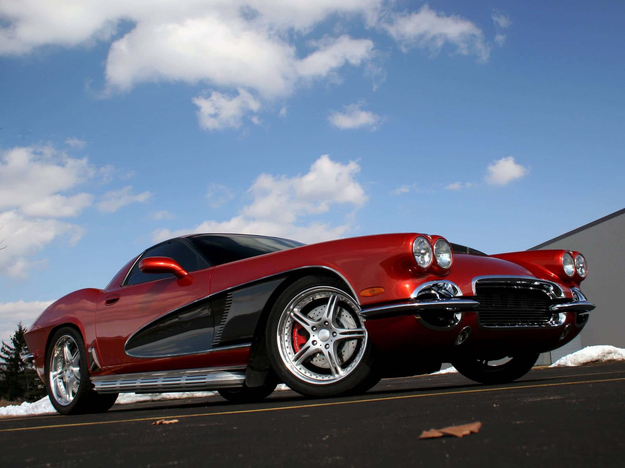 classic 桌布 壁紙 — 一輛亮紅色的經典Corvette跑車停在積雪的路邊，天空湛藍，白雲朵朵。