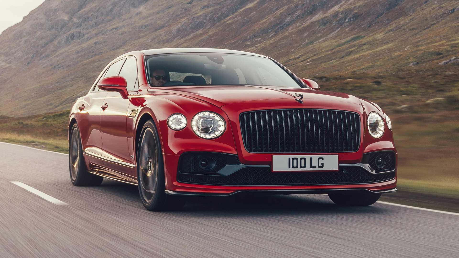 Bentley Flying Spur 桌布 壁紙 — 一輛亮紅色的賓利 Flying Spur 在蜿蜒的山路上疾馳，背景模糊。